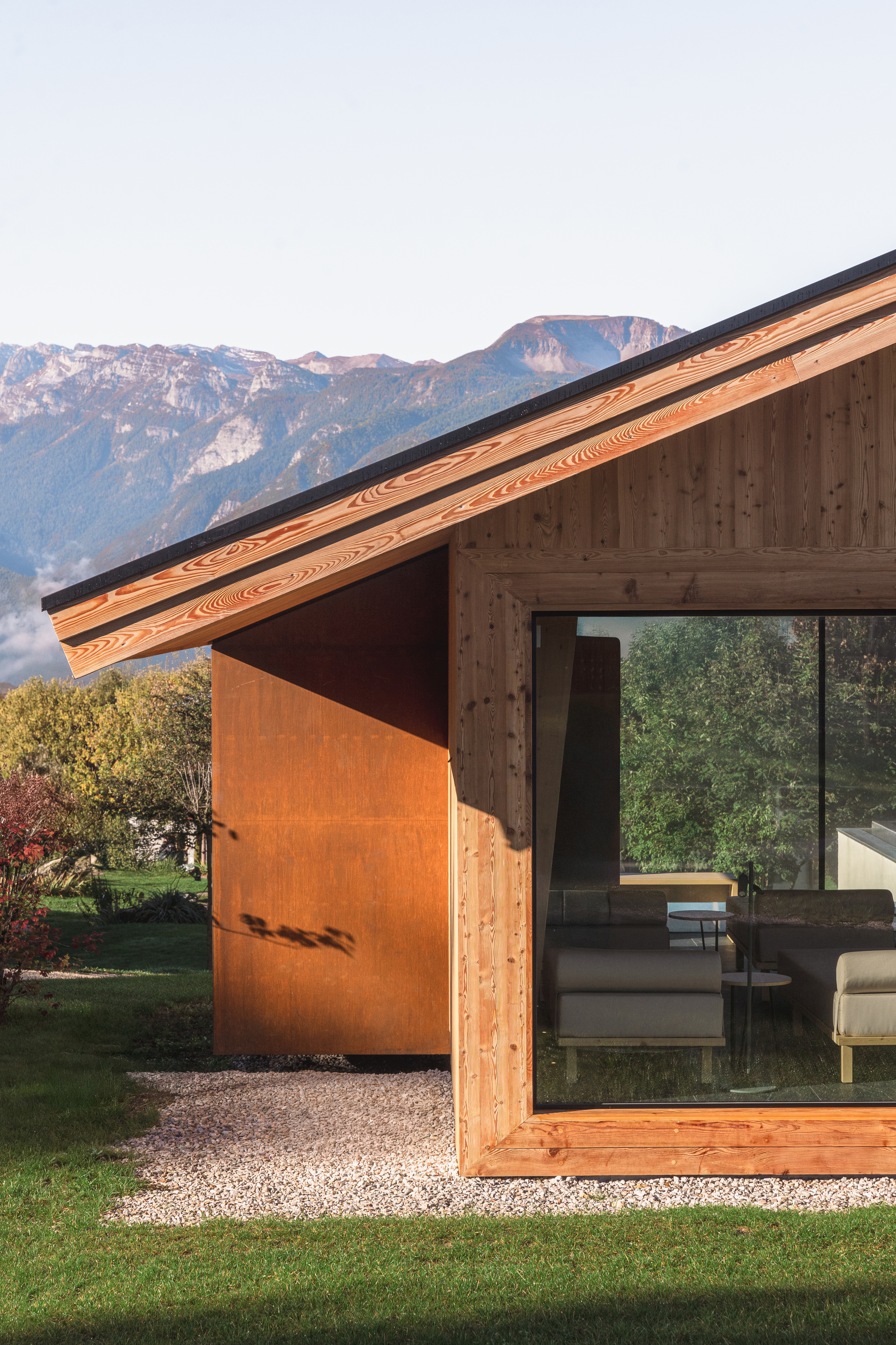 Exterior view of the timber and weathered steel pavilion with glazed corner against a mountain backdrop