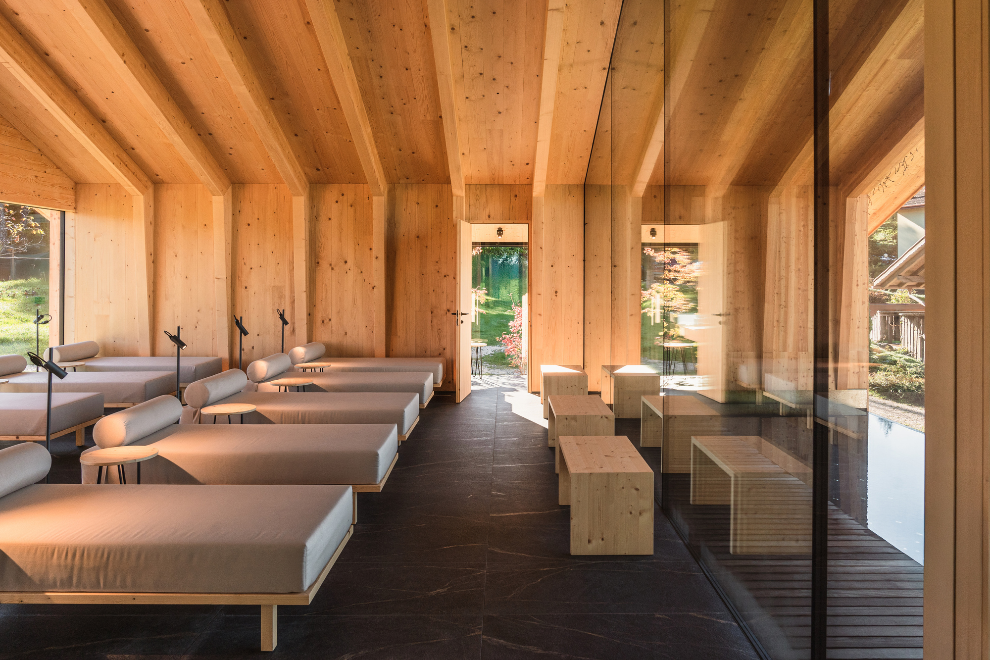 Spa room with timber gabled ceiling, treatment beds on dark tile floor, and sauna boxes along glazed wall