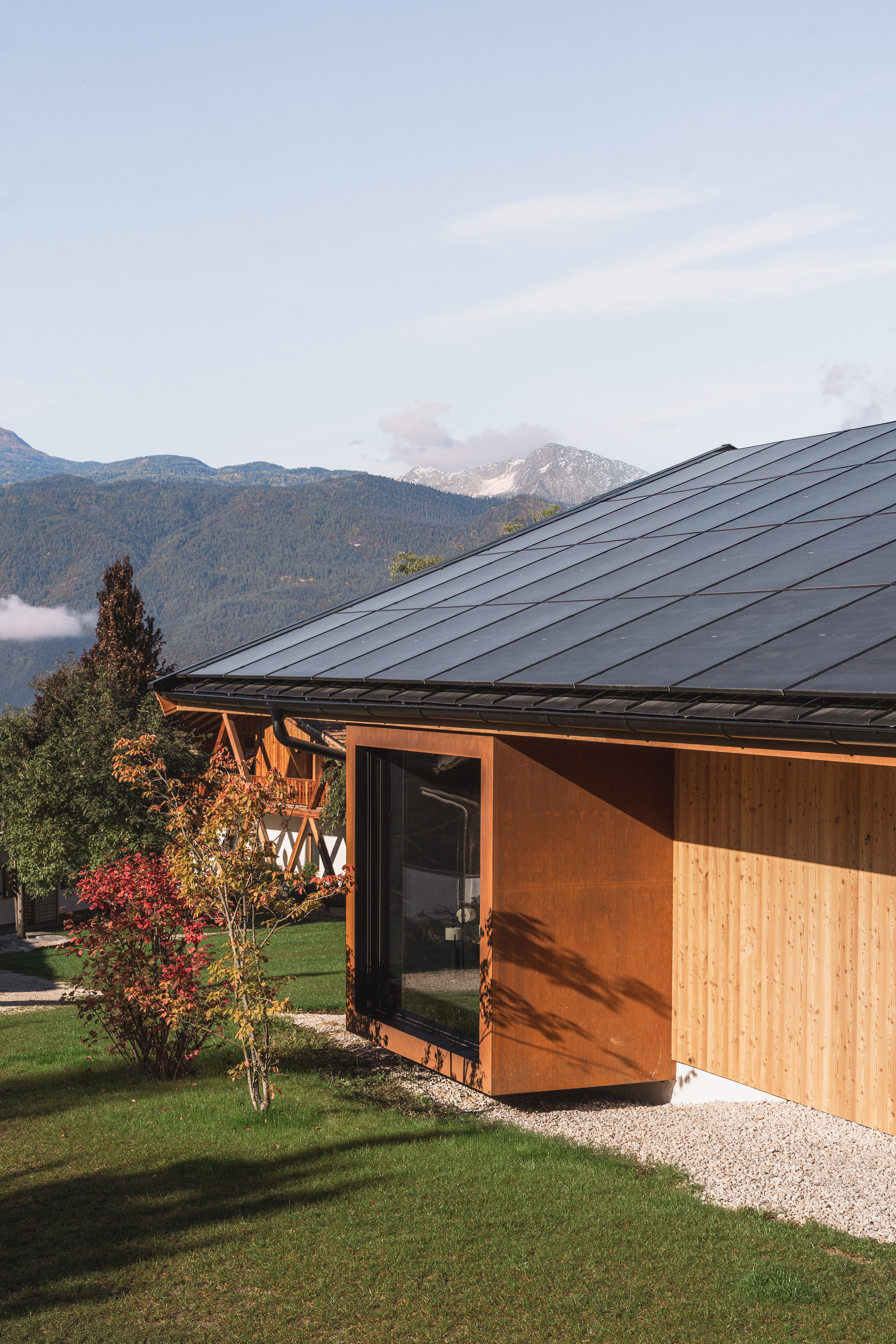 Cantilevered weathered steel volume with timber cladding beneath a dark metal roof at dusk