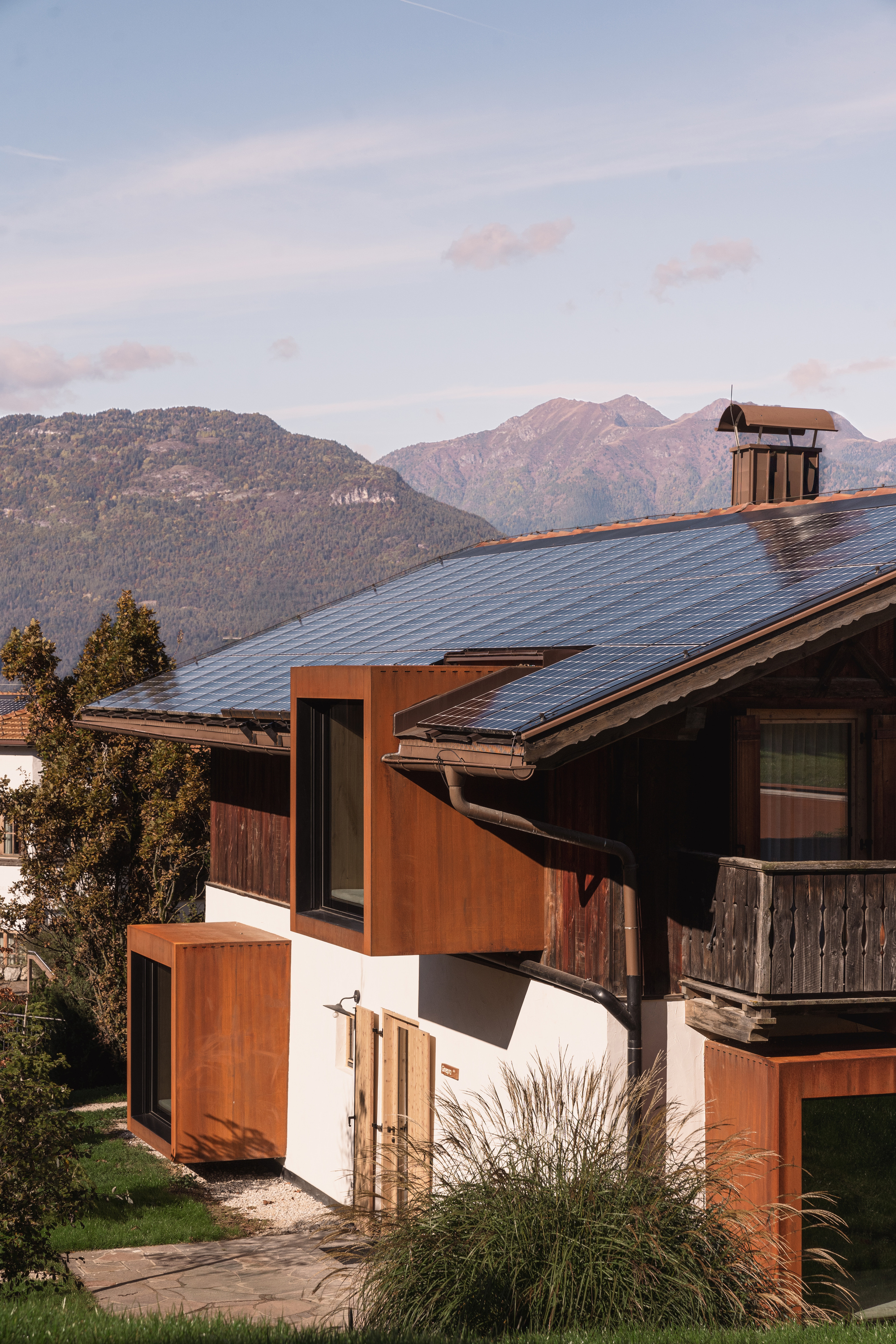 Composition of sloped metal roofs and weathered steel volumes interlocking with white stucco walls at sunset
