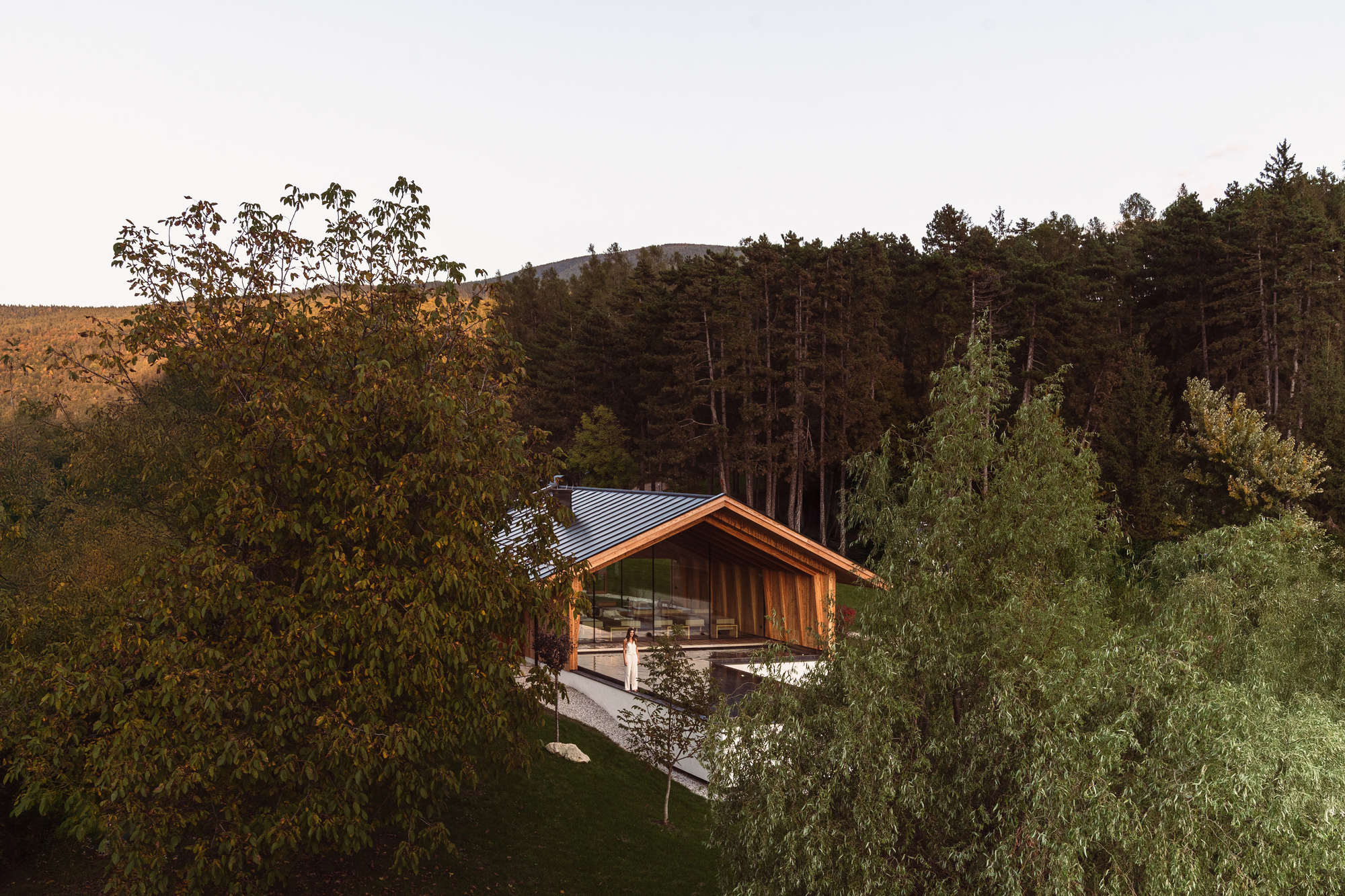 Gabled timber structure with metal roof nestled into a forested hillside at sunset