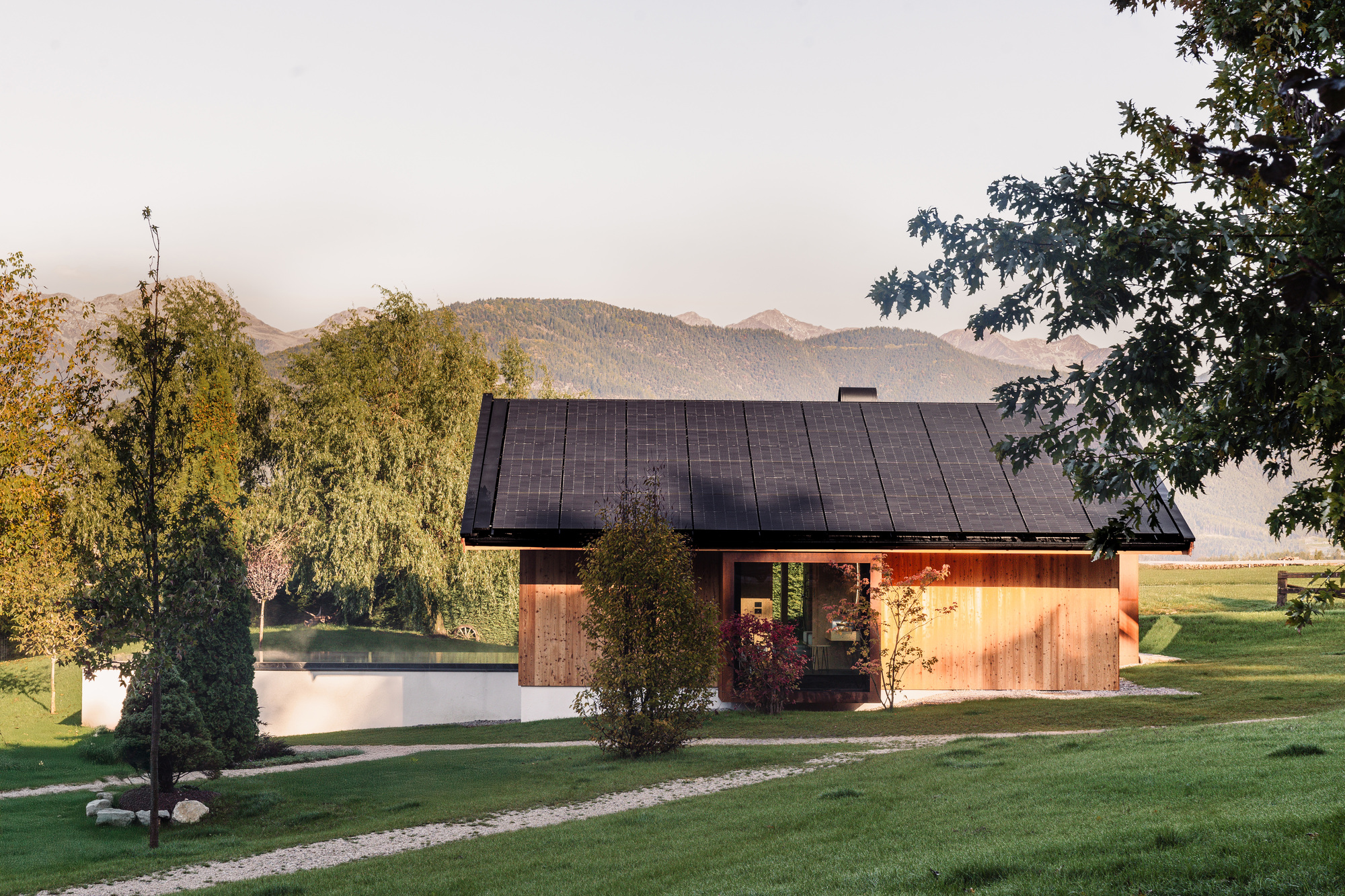 Low-pitched gabled house with metal roof and timber cladding beside a pond in evening light