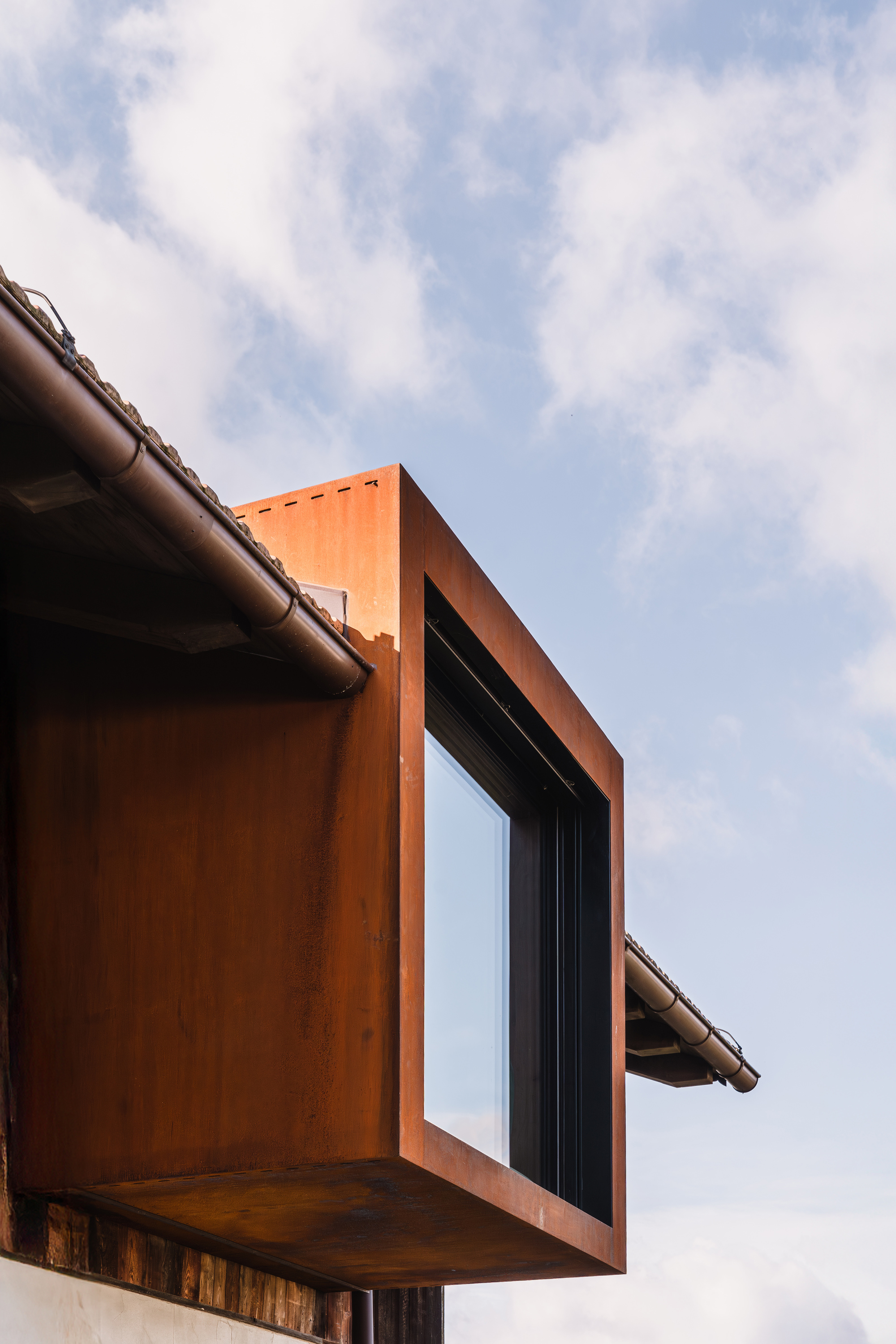 Cantilevered weathered steel bay window framed against a cloudy sky