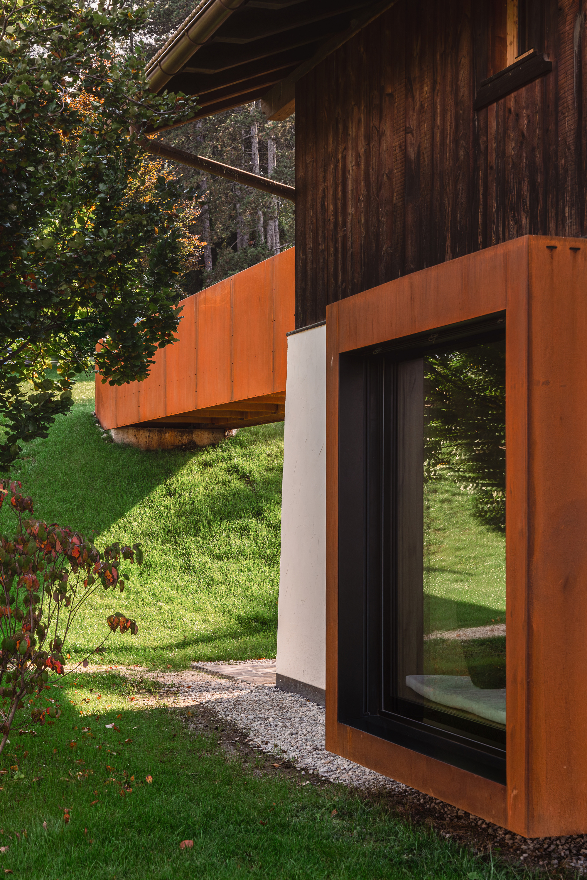 Weathered steel frame wrapping a full-height window opening in the timber facade
