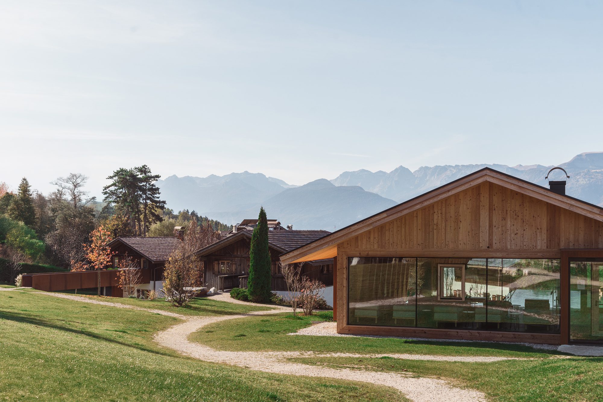 Cluster of gabled timber volumes with glazed walls set in a meadow with mountain views