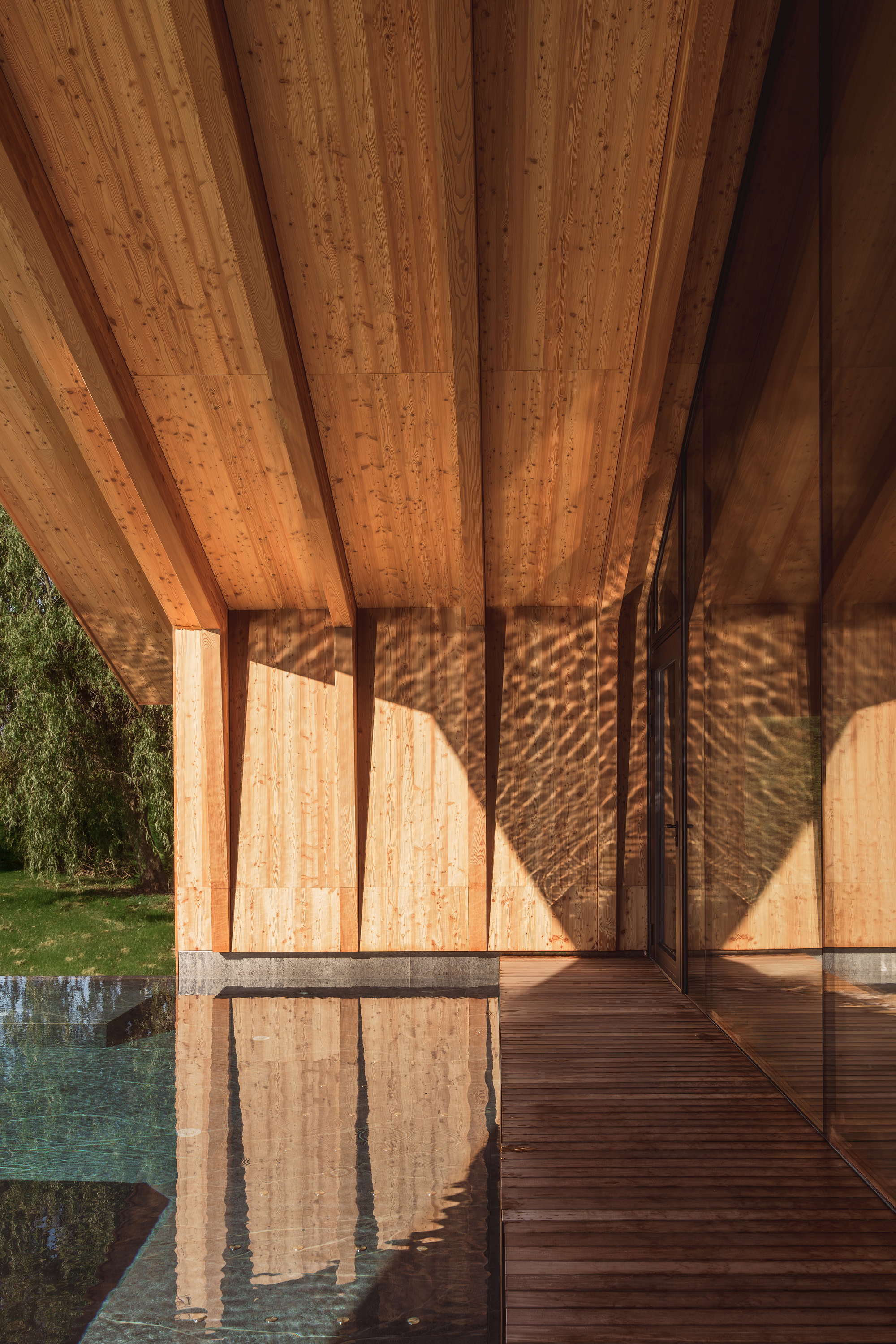 Covered timber deck with exposed wood ceiling and reflecting pool at golden hour