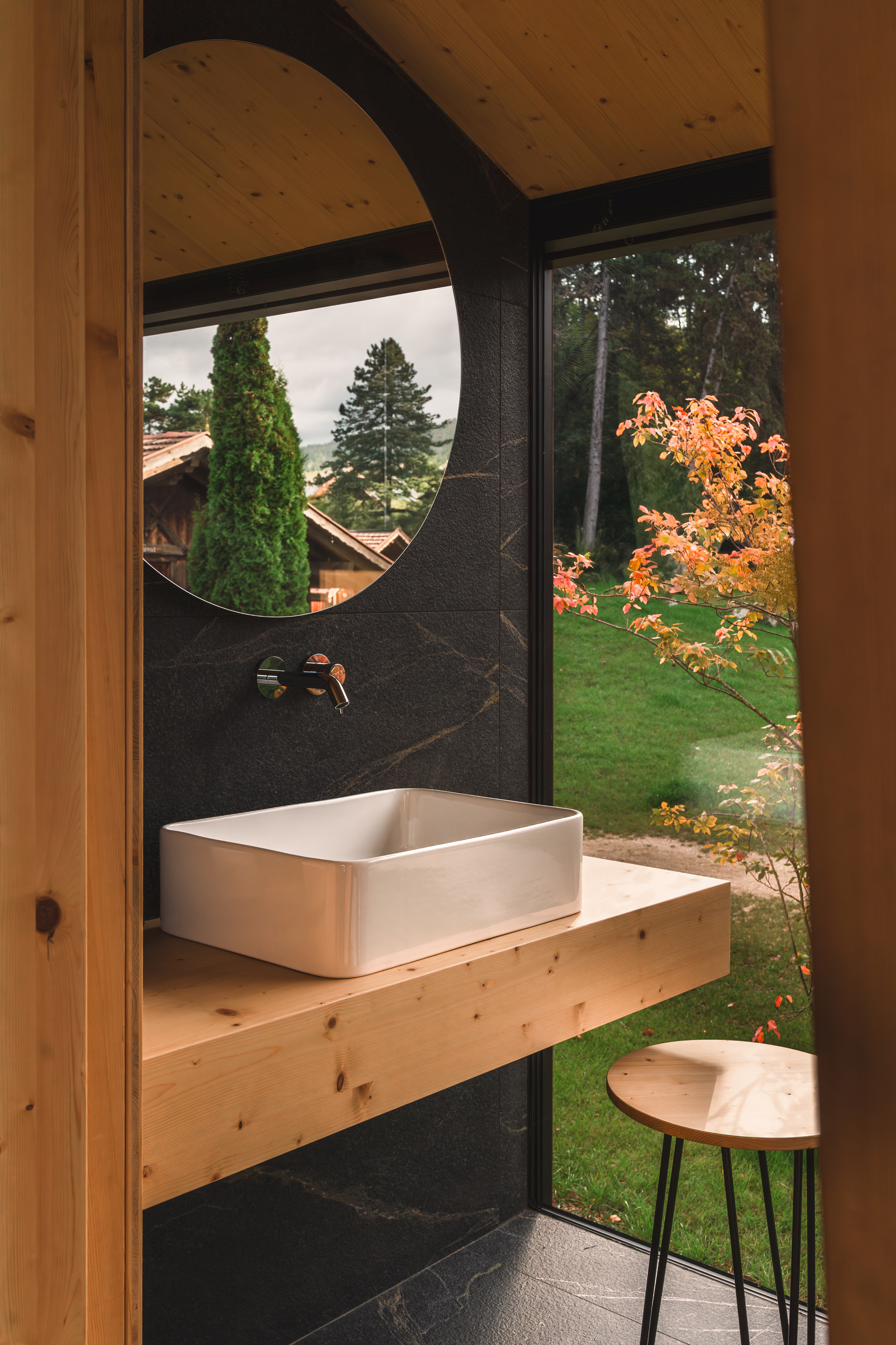 Floating timber vanity with vessel sink and circular mirror against dark stone wall
