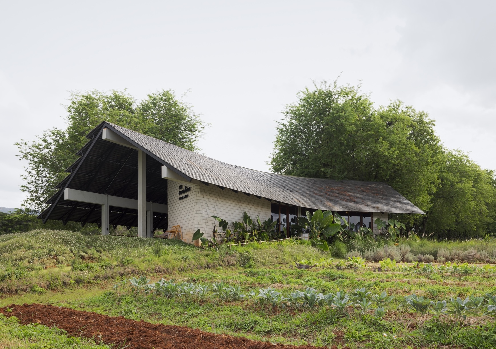 Pitched roof pavilion with brick walls and exposed timber frame amid cultivated vegetable plots
