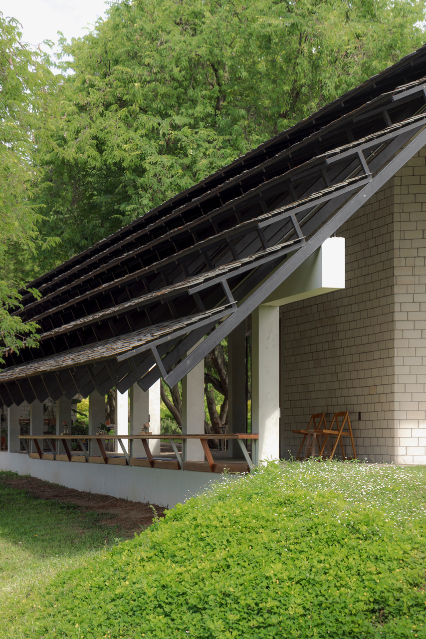 Corner detail of exposed roof structure with timber rafters and white columns beside flowering groundcover