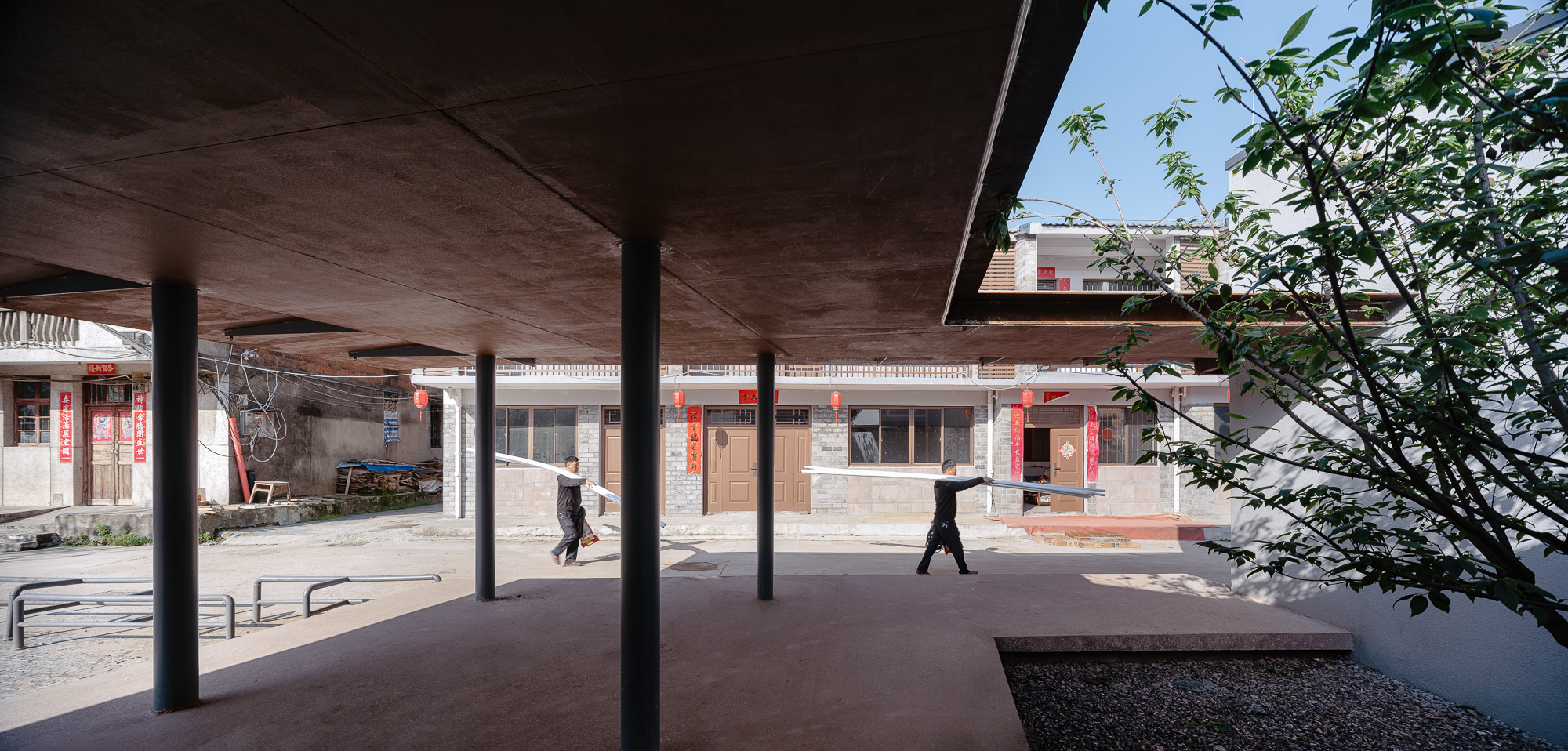 View through the pavilion's timber-lined ceiling toward surrounding residential buildings with pedestrians crossing the plaza