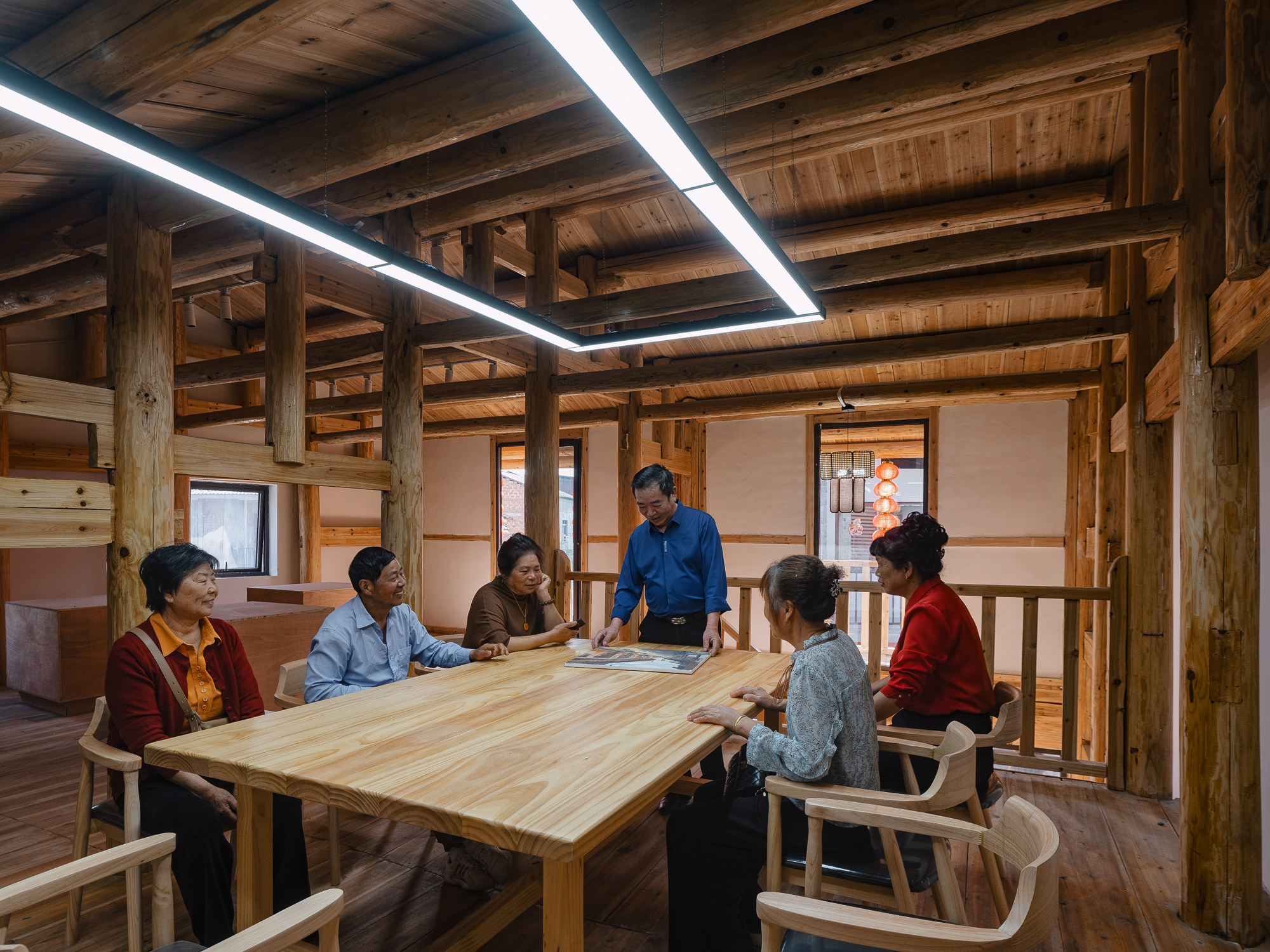 Interior meeting room with exposed timber post-and-beam structure and linear skylights illuminating a group at the table