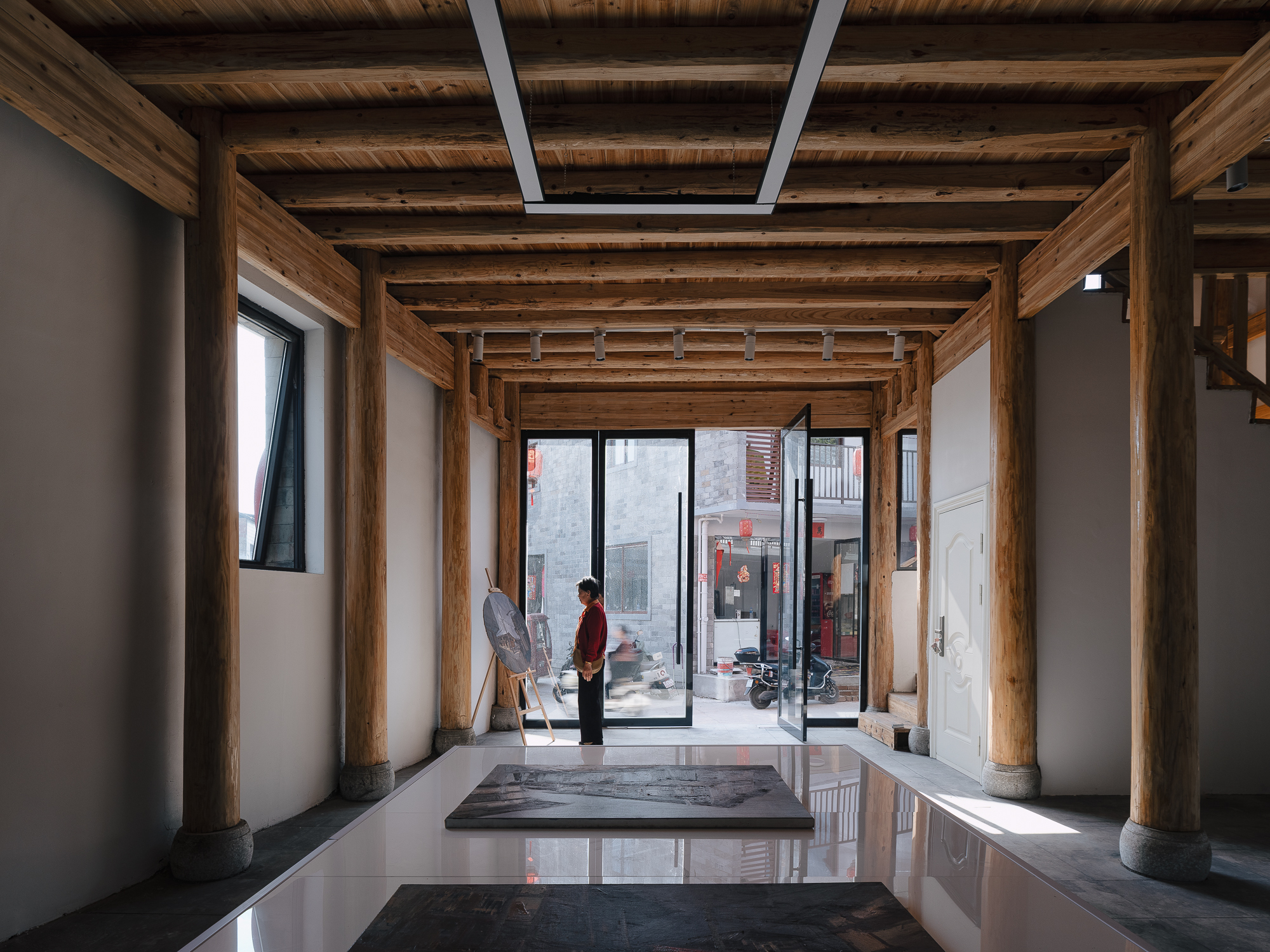 Interior hall with exposed timber columns and beams, polished floor and two figures in conversation