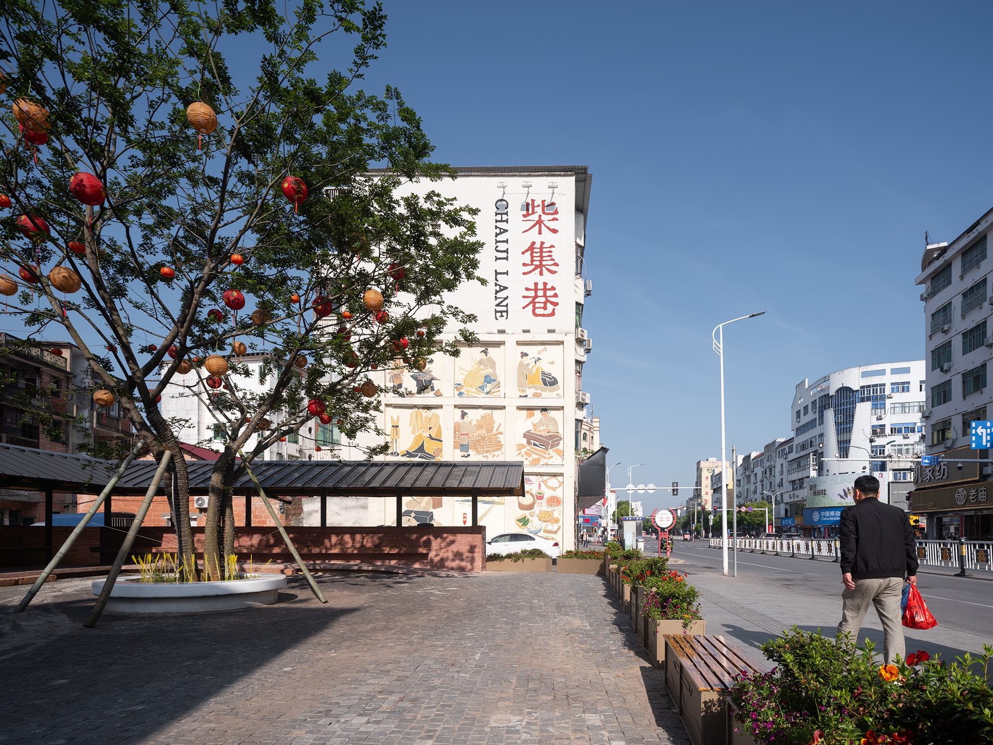 Street corner pavilion with decorative tree and planted beds beside a pedestrian crossing