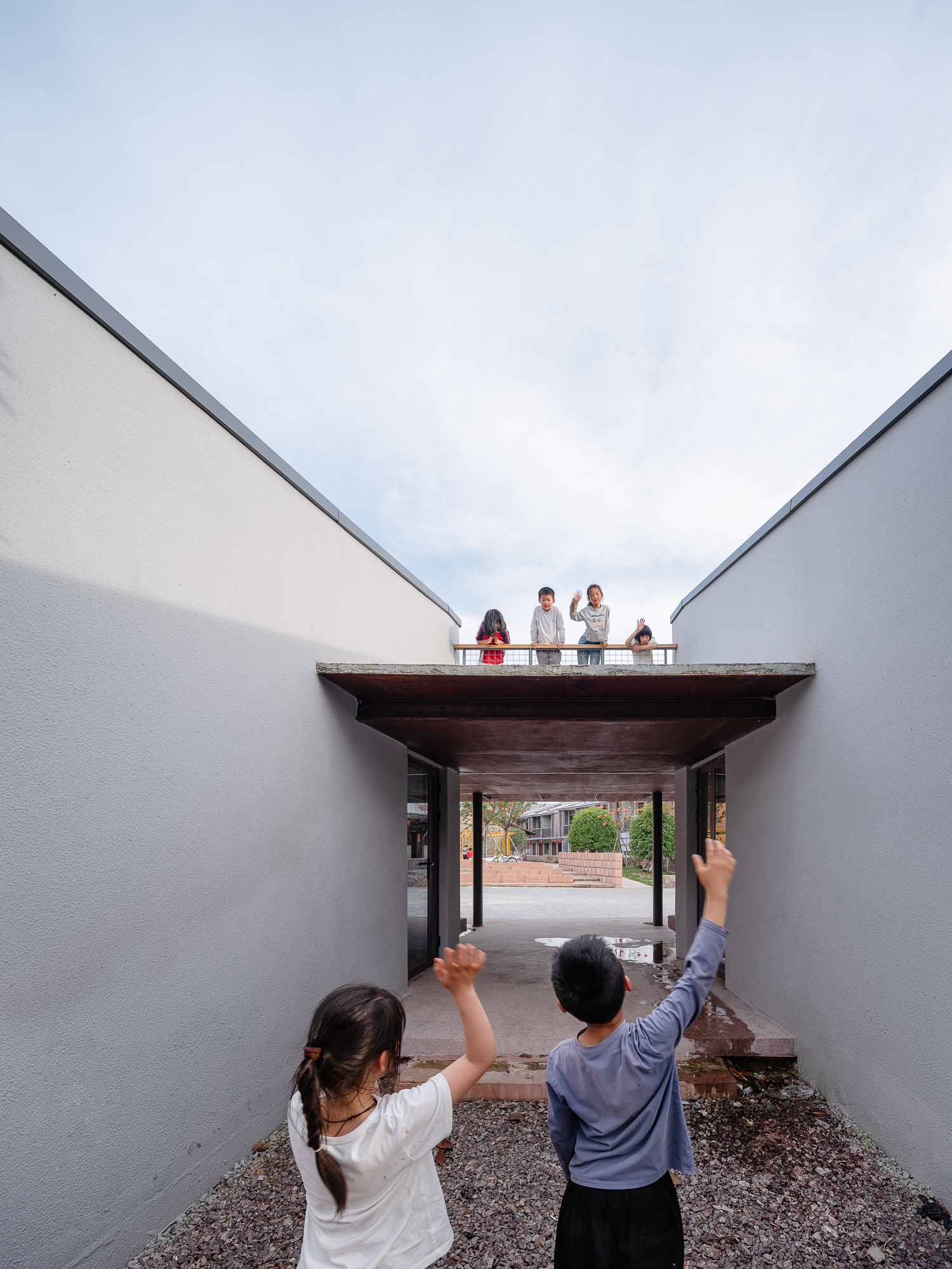 Courtyard view through a timber-roofed passageway with people standing on the rooftop terrace above