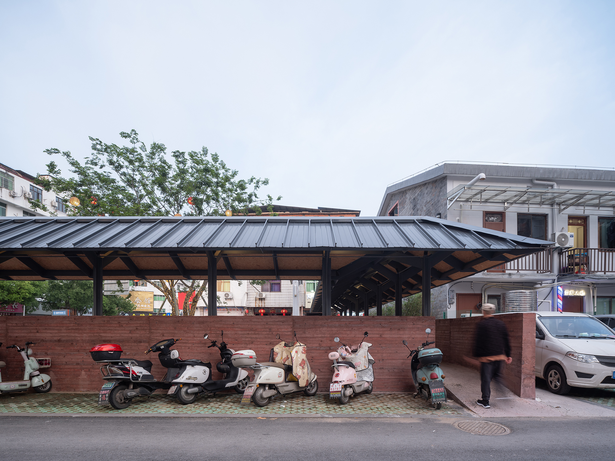 Standing seam metal roof pavilion with exposed timber trusses and parked scooters along the street