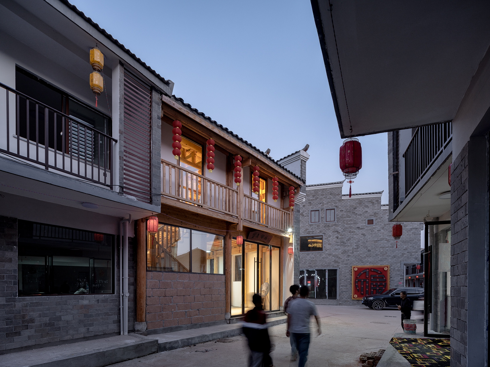Narrow pedestrian lane between timber-framed building with red lanterns and grey brick structures at dusk