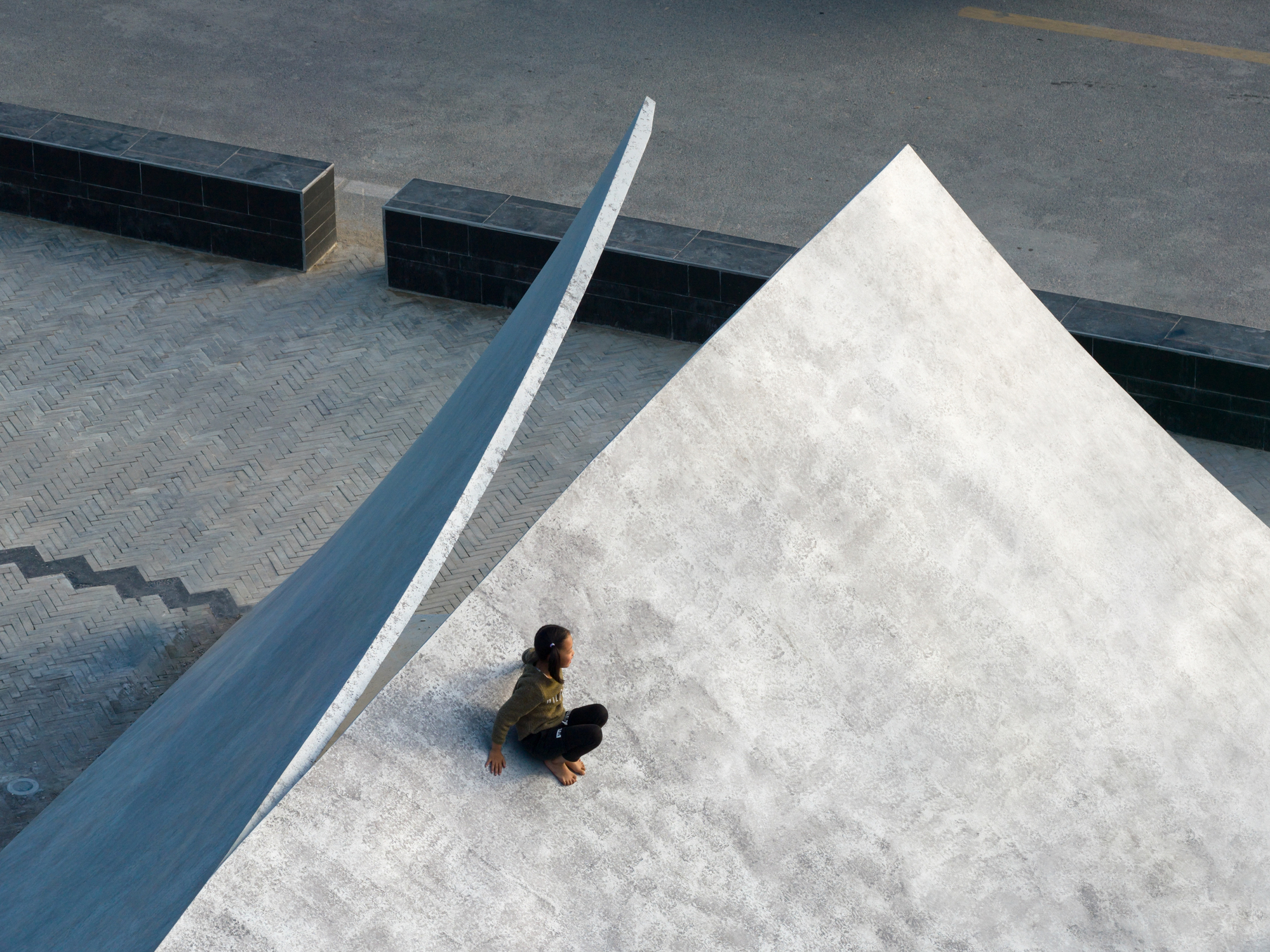 Person sitting on the sloped concrete plane beside the ridge line casting sharp shadow