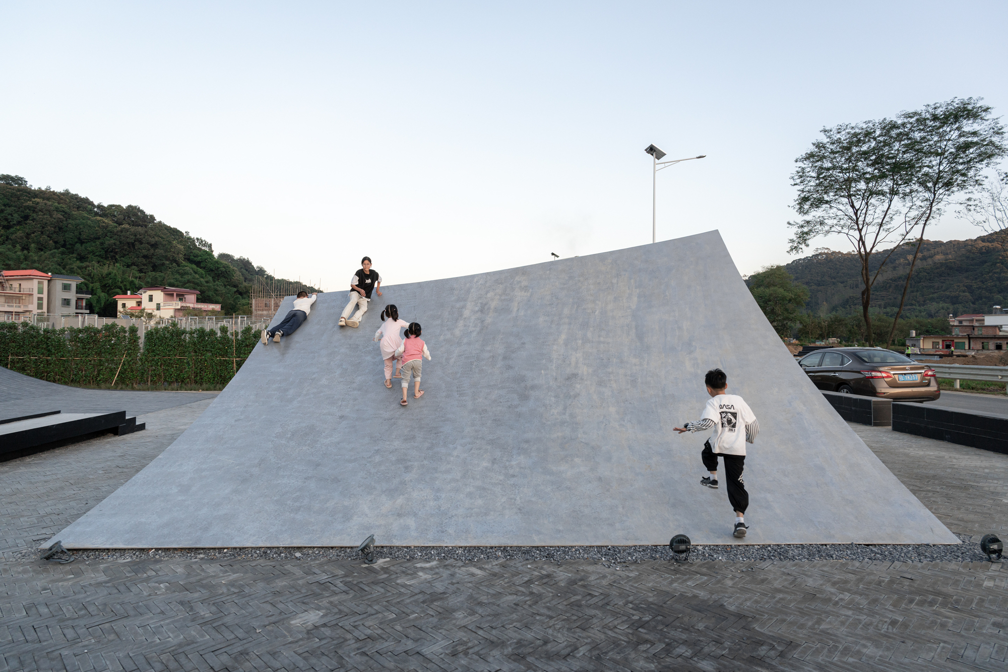 Children climbing the inclined concrete roof surface at twilight with hills in the background