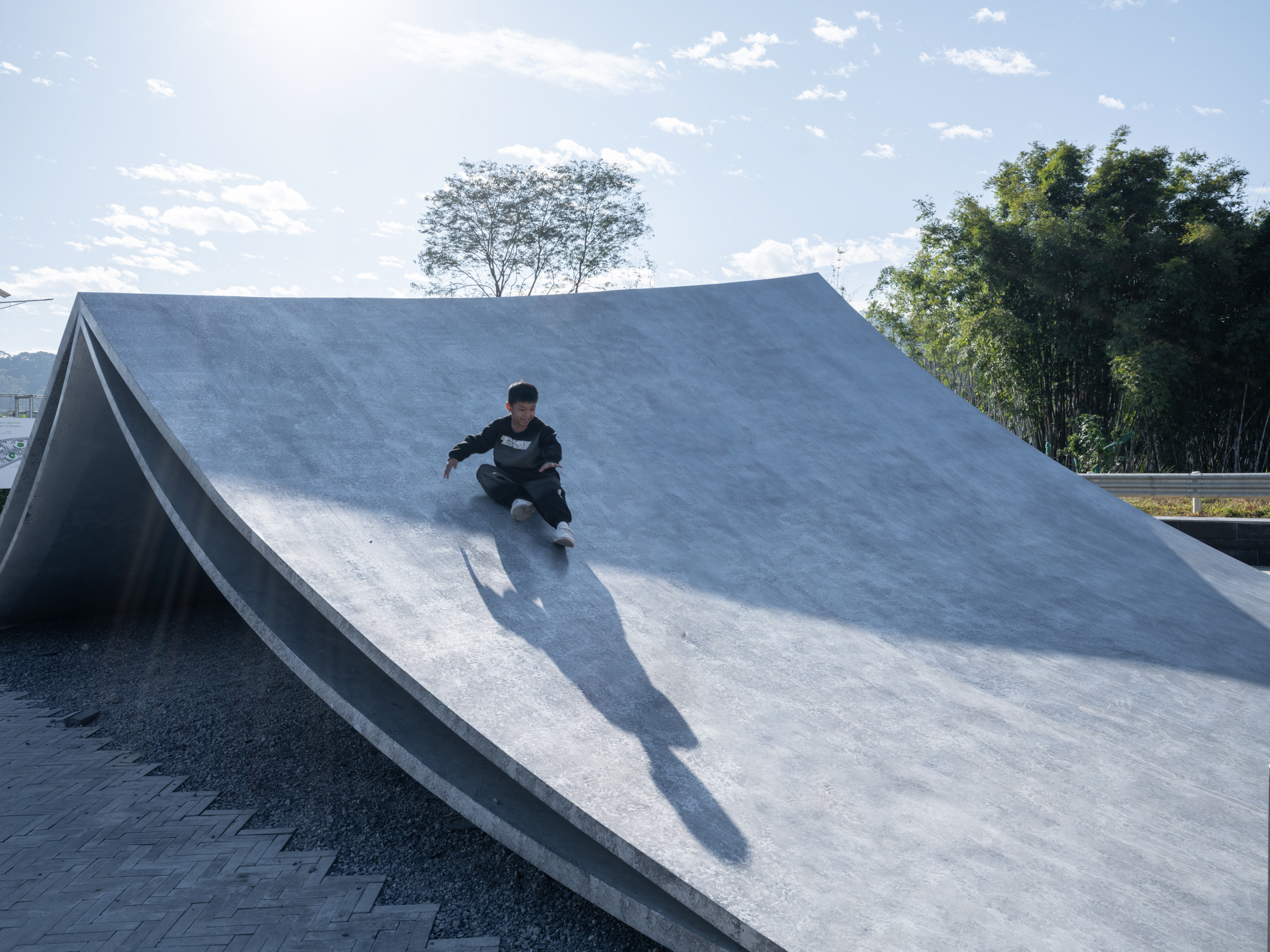 Concrete skateable ramp with a skateboarder descending under afternoon sun and scattered clouds