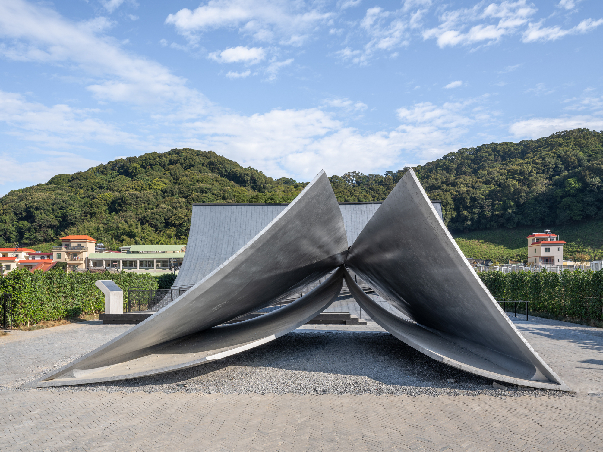 Three intersecting peaked concrete planes forming a shelter against forested hills