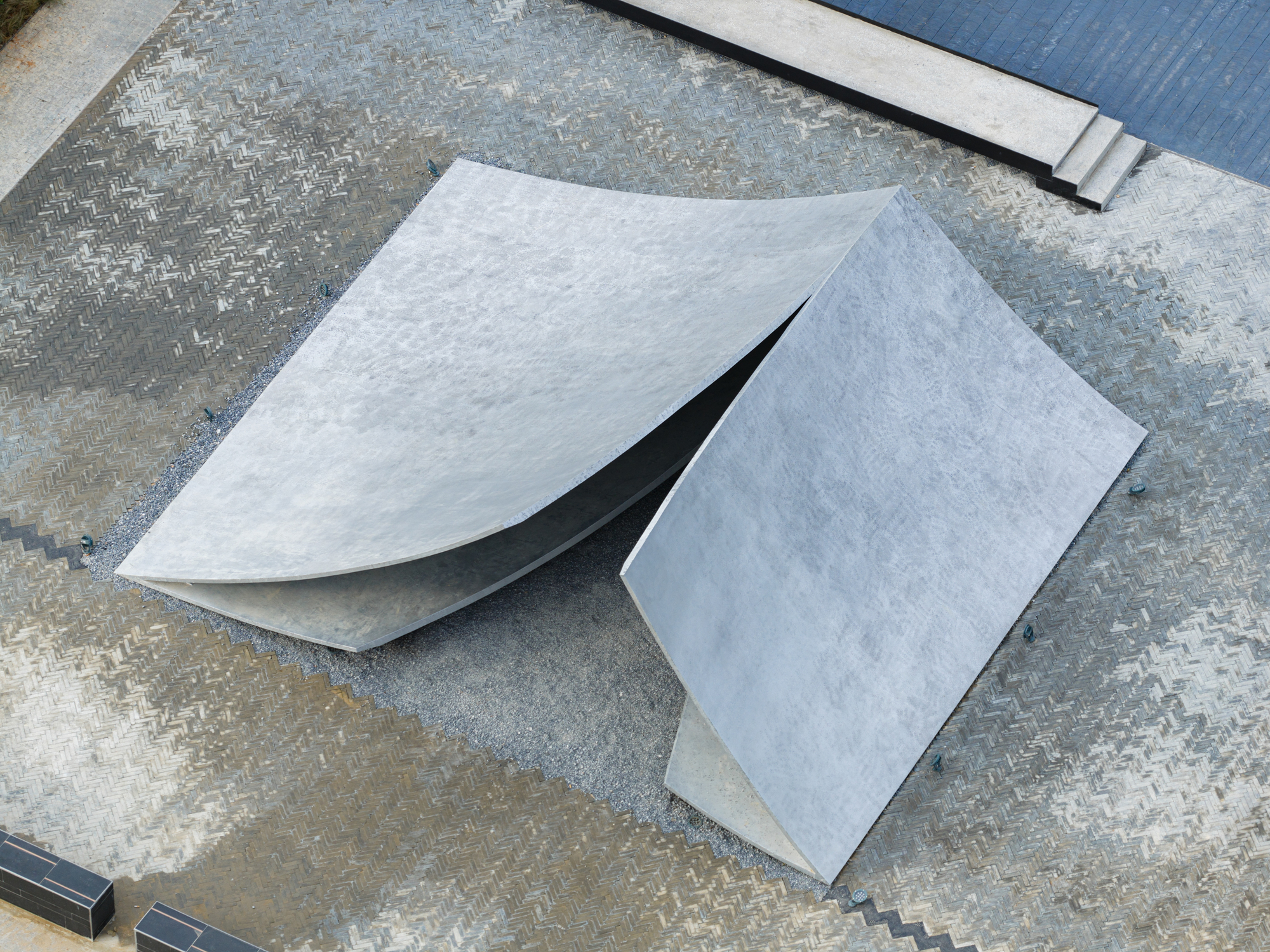 Overhead view of folded concrete planes meeting at sharp angles on a patterned paving