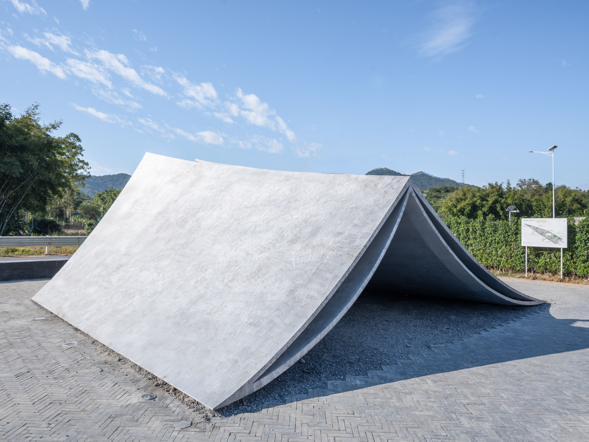 Tent-like concrete structure with one light plane and one dark plane under midday sun