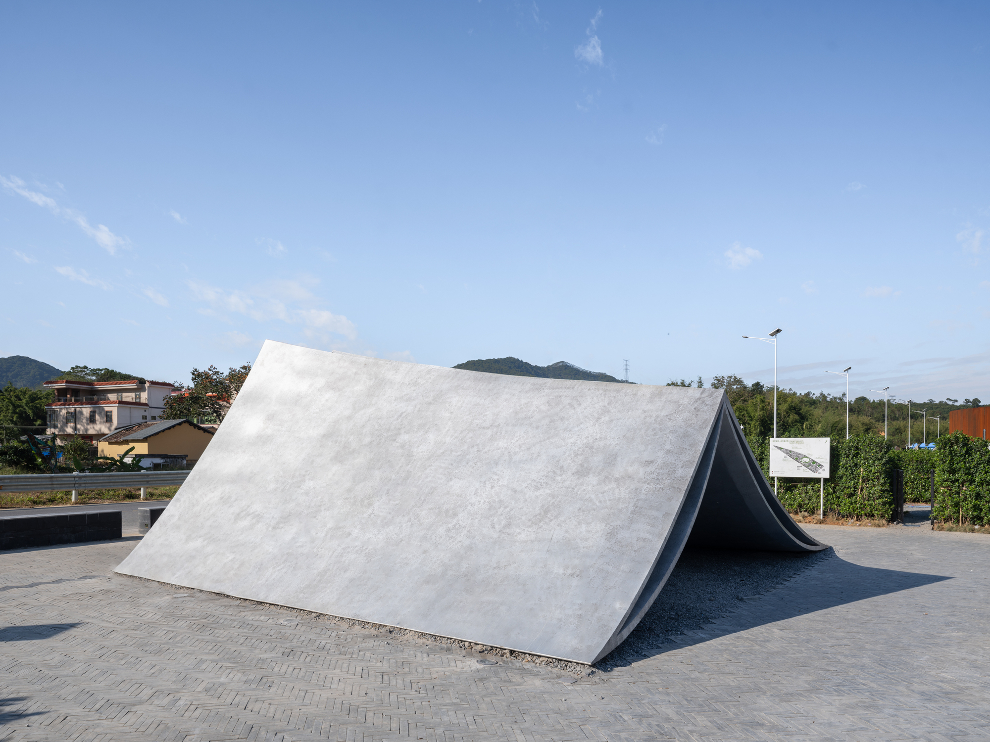Folded concrete pavilion with white and black surfaces beside a roadway at dusk