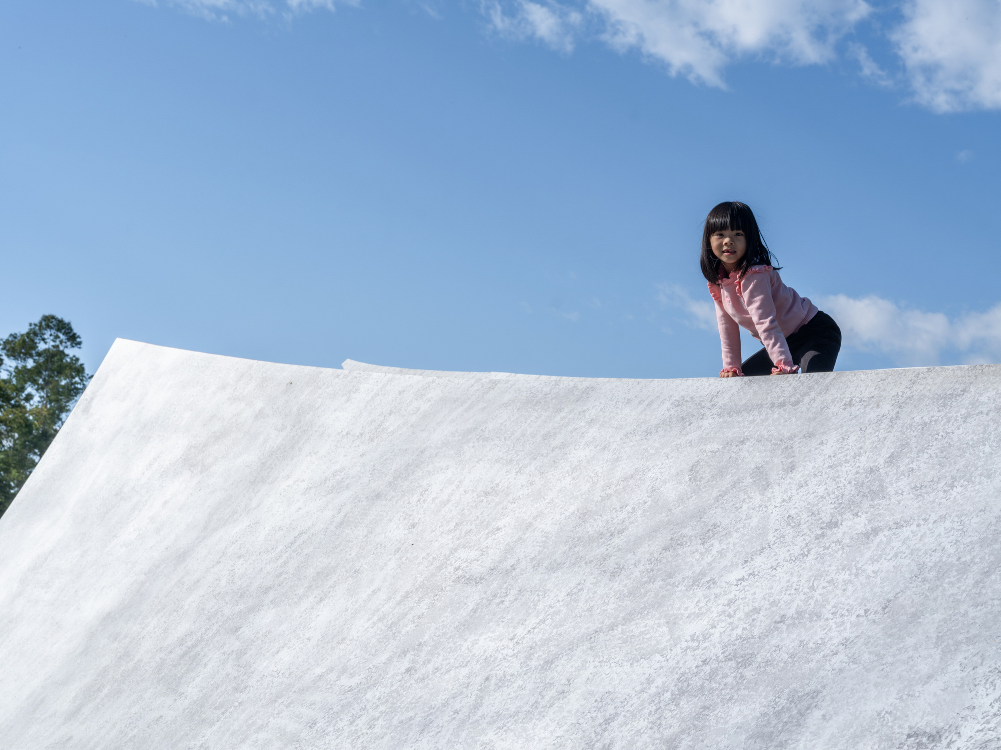 Child crawling up the textured concrete roof slope under a clear blue sky