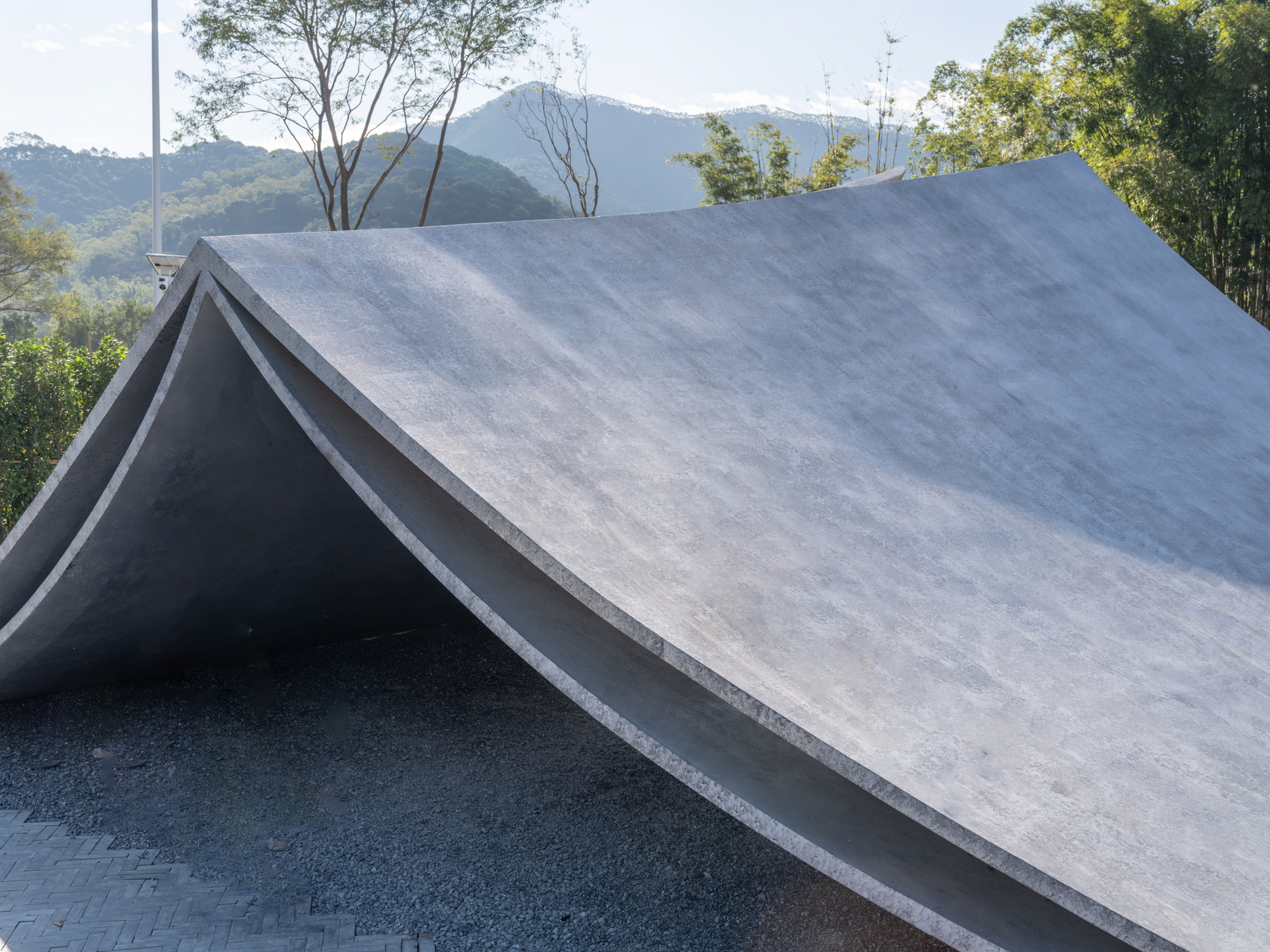 Angular concrete roof with folded planes set against forested mountains under daylight
