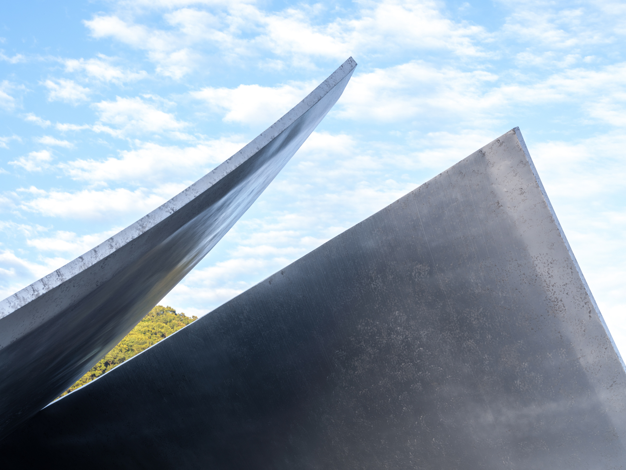 Close-up of two intersecting concrete roof planes meeting at a sharp edge beneath clouds