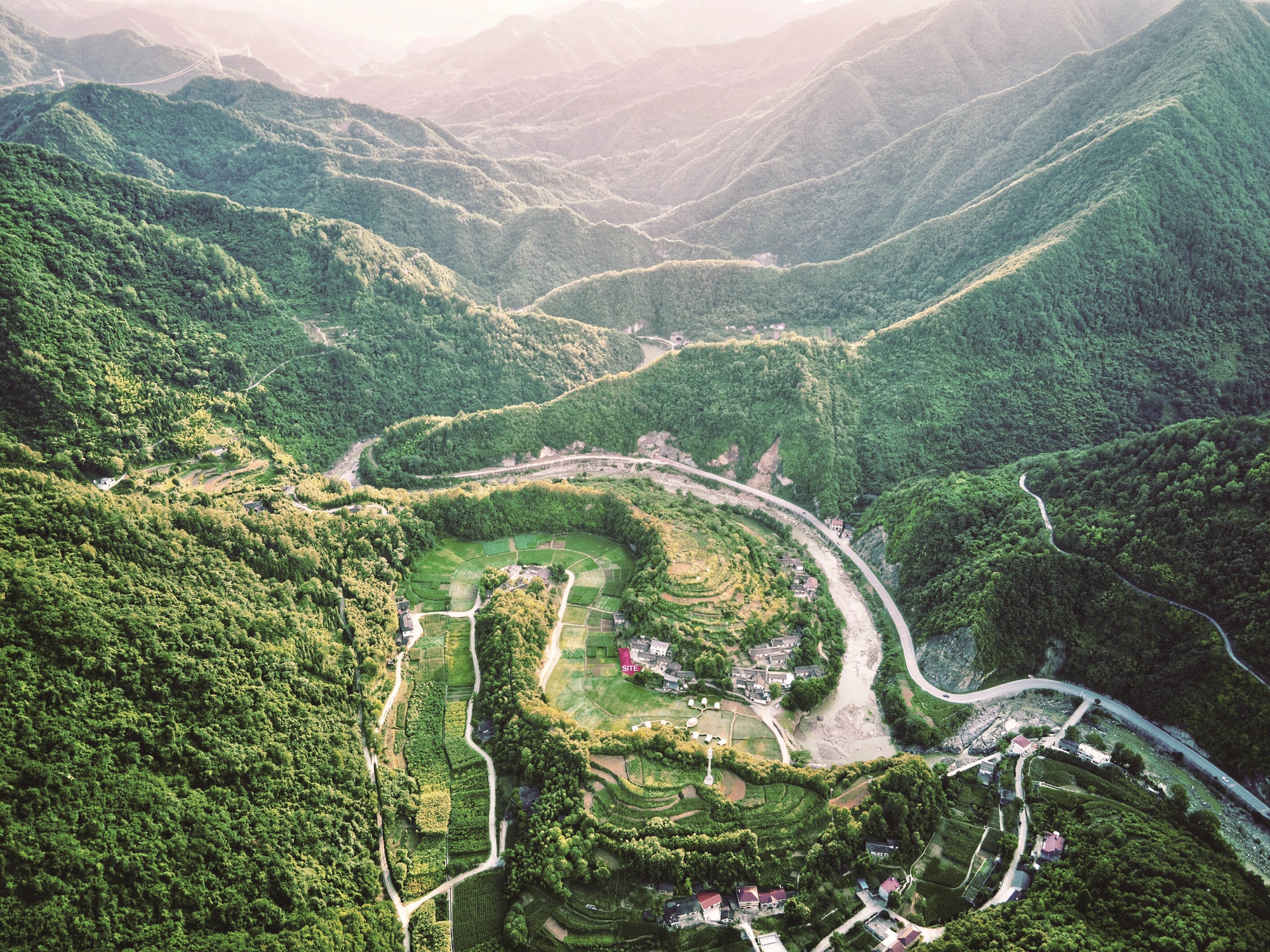 Aerial view of terraced agricultural fields and clustered buildings nestled in a forested mountain valley