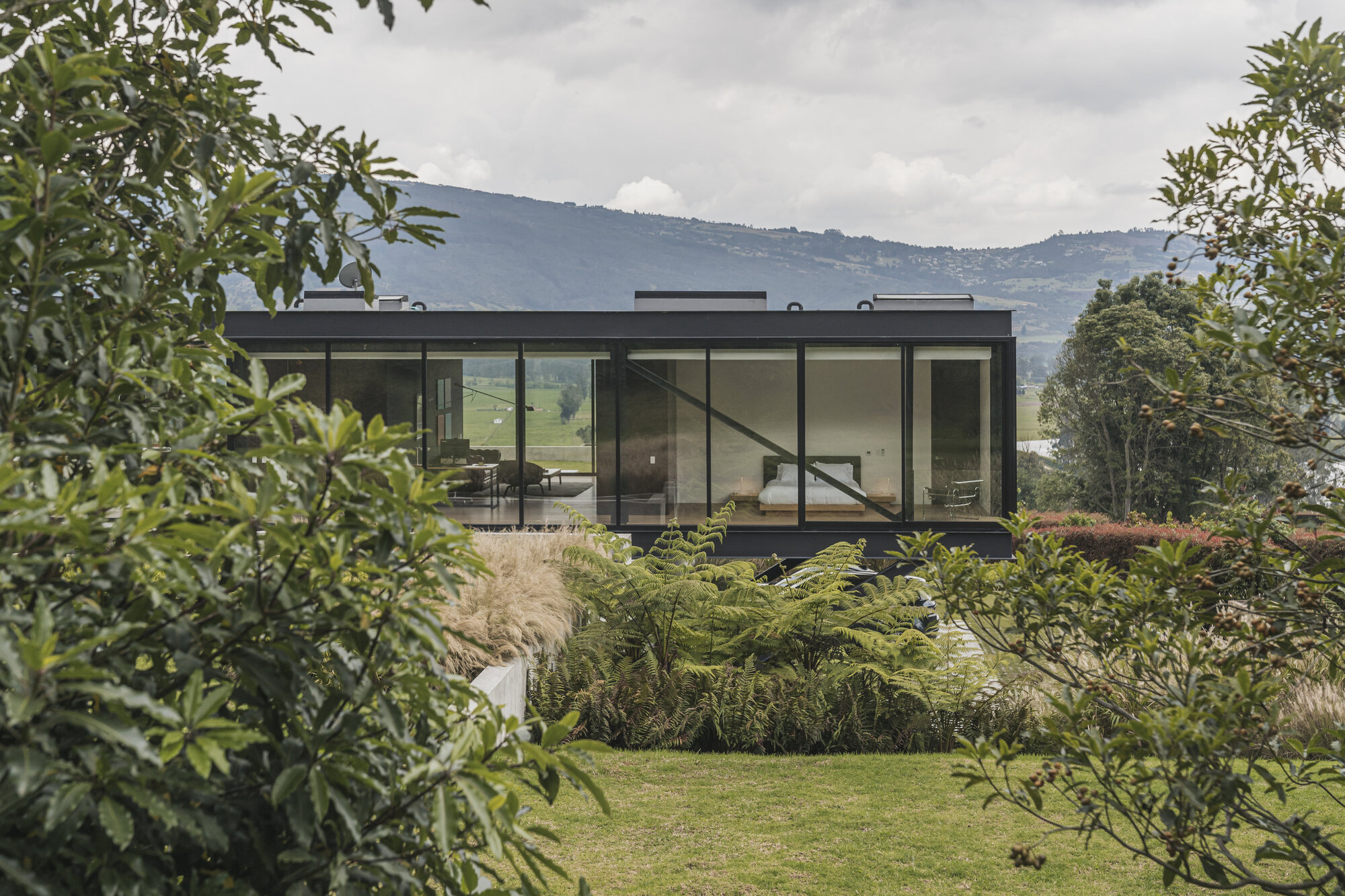 Glass-walled pavilion set in a landscaped garden with mountains visible in the distance