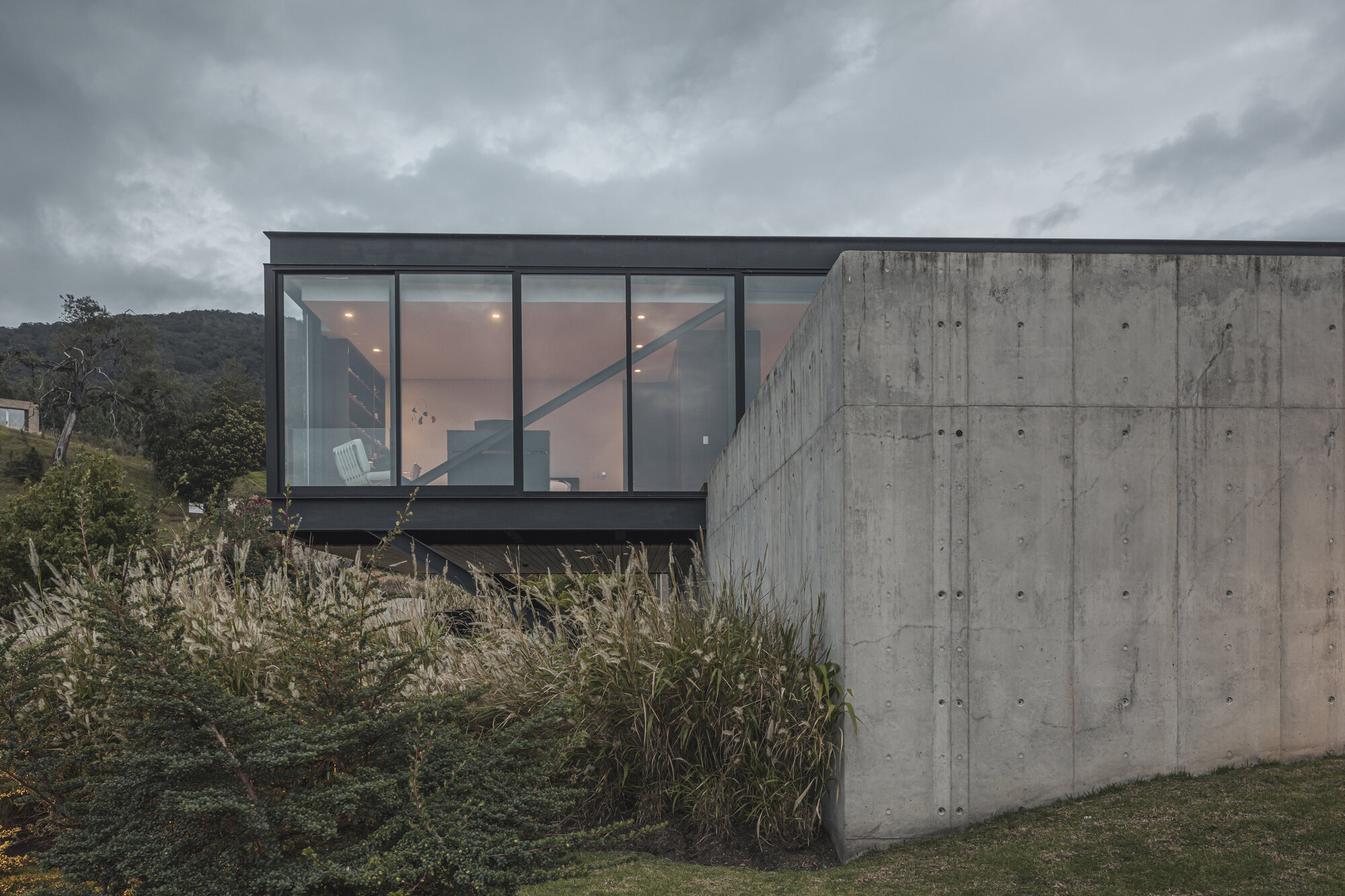Board-formed concrete retaining wall rising from a grassy slope at dusk