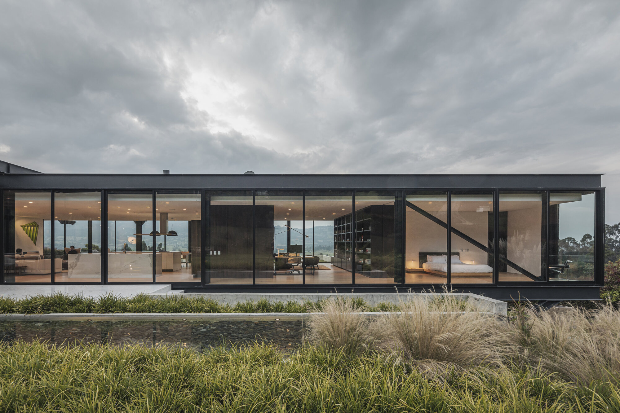 Long facade of floor-to-ceiling glazing with black frames and diagonal bracing behind ornamental grasses