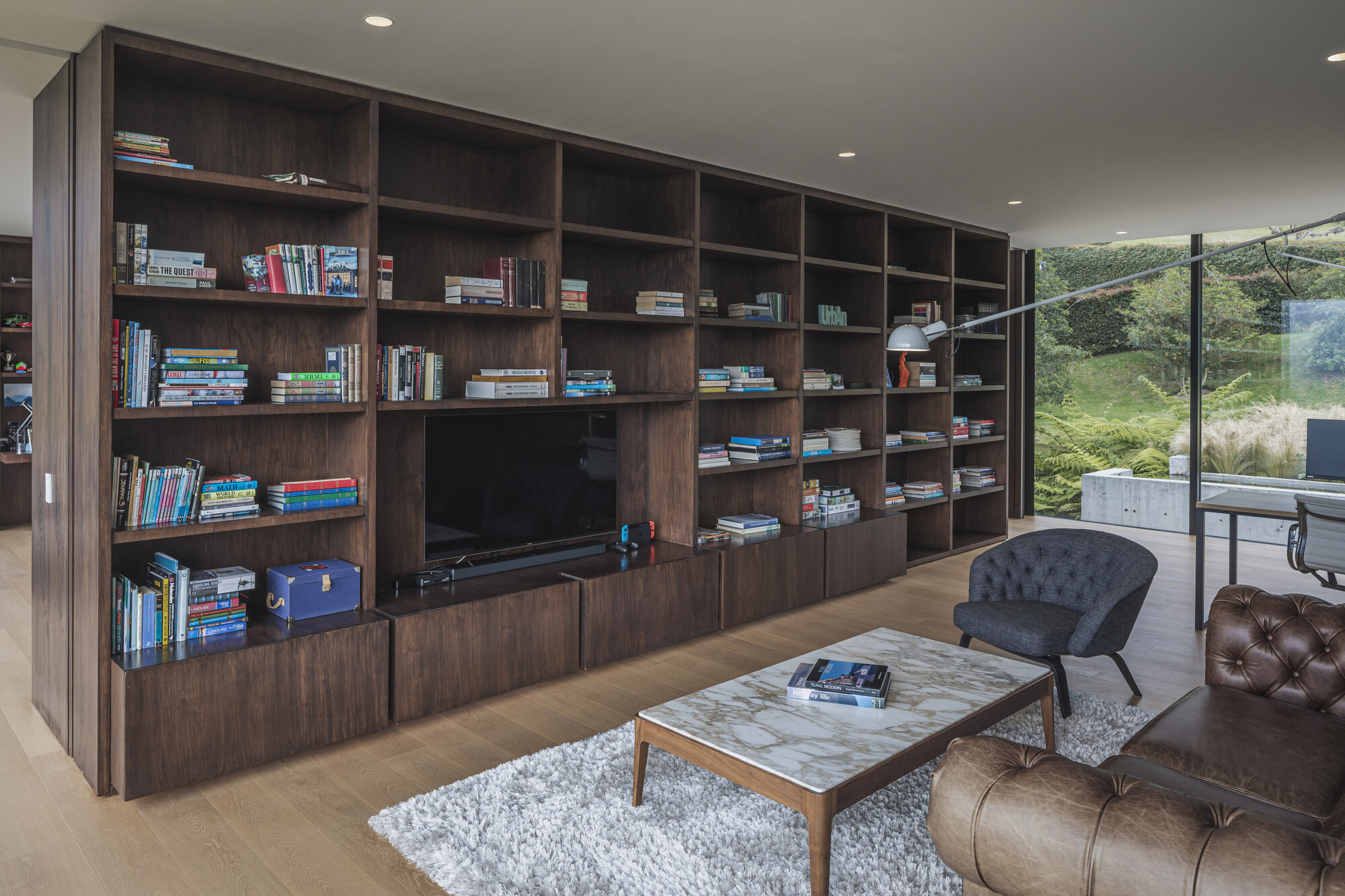 Dark timber shelving wall with integrated television overlooking a planted courtyard through glazed doors