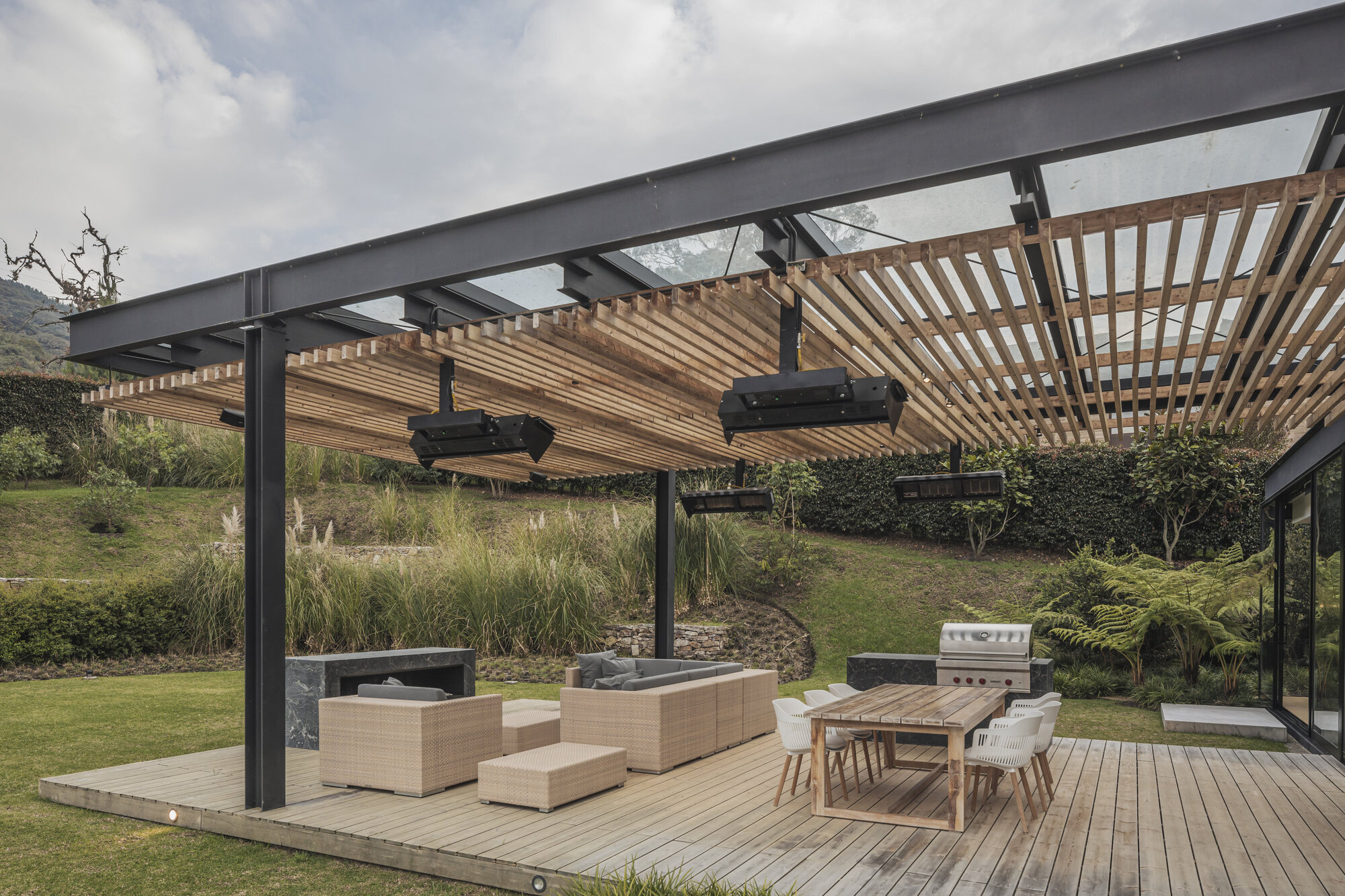 Outdoor terrace with timber slat pergola supported by steel columns under cloudy skies