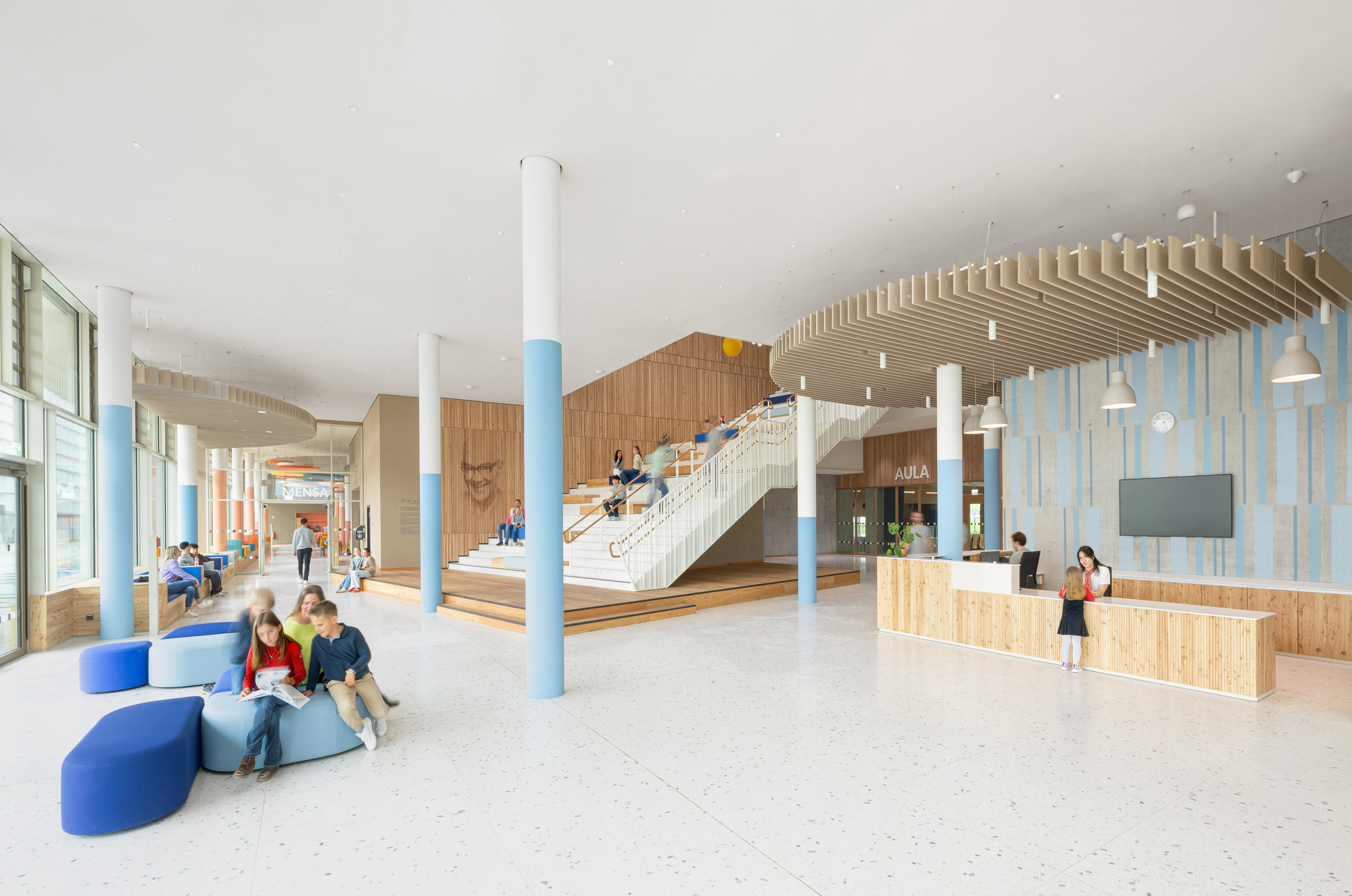 Entry lobby with timber reception desk, slatted ceiling feature, and white columns with blue bases