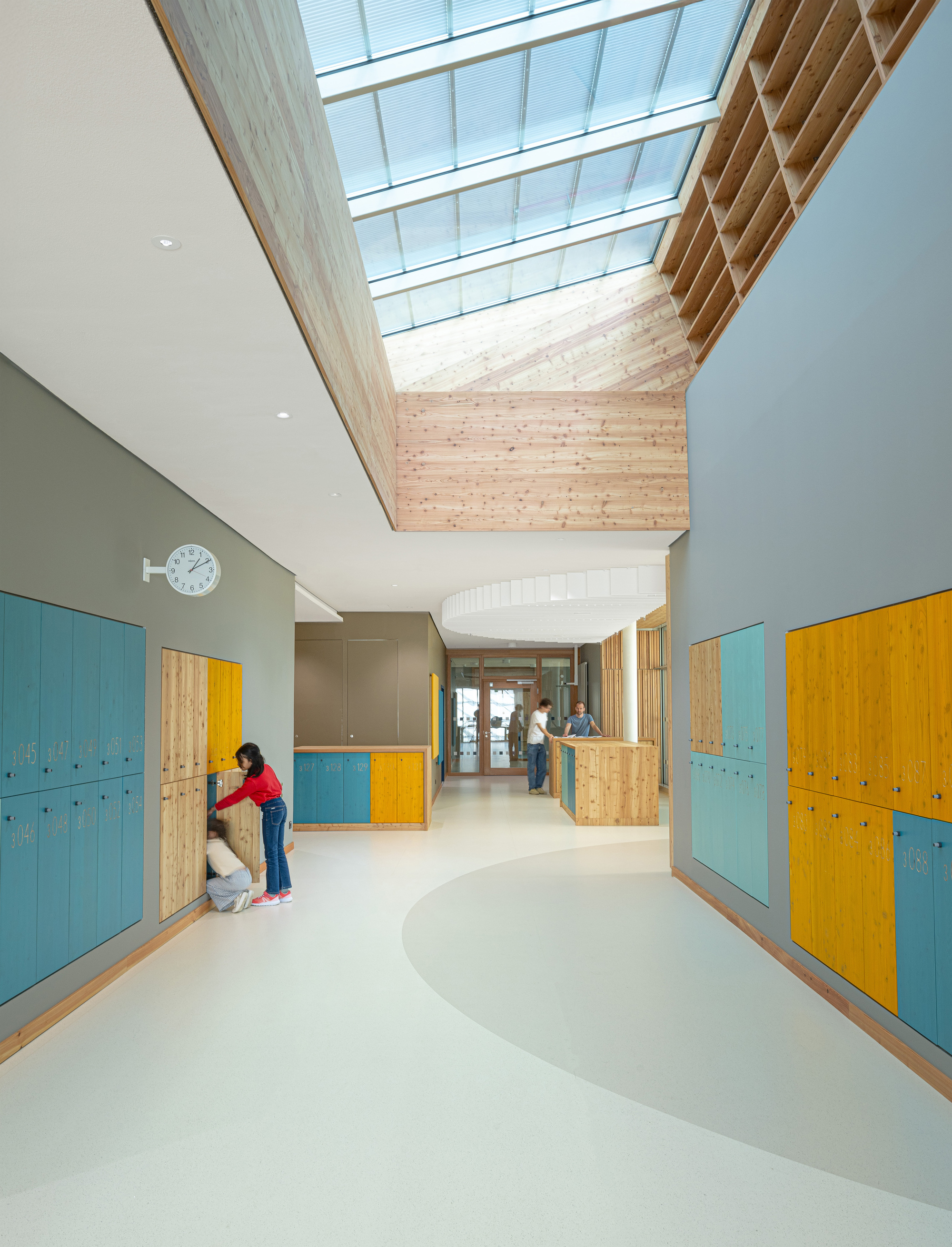 Curved hallway beneath a timber-framed skylight with painted and natural wood lockers lining both sides