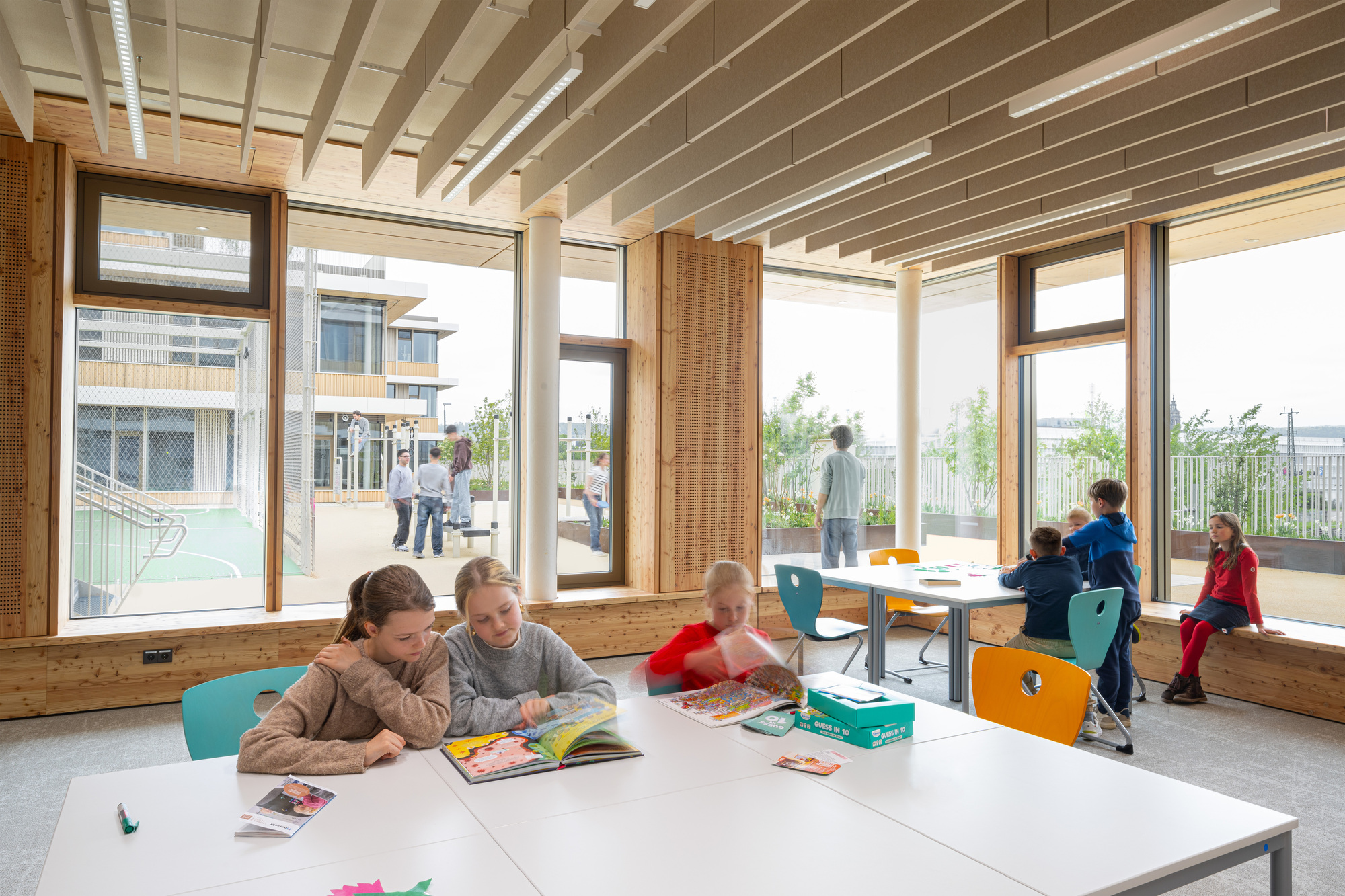 Classroom with exposed timber ceiling rafters, floor-to-ceiling windows and children at white tables