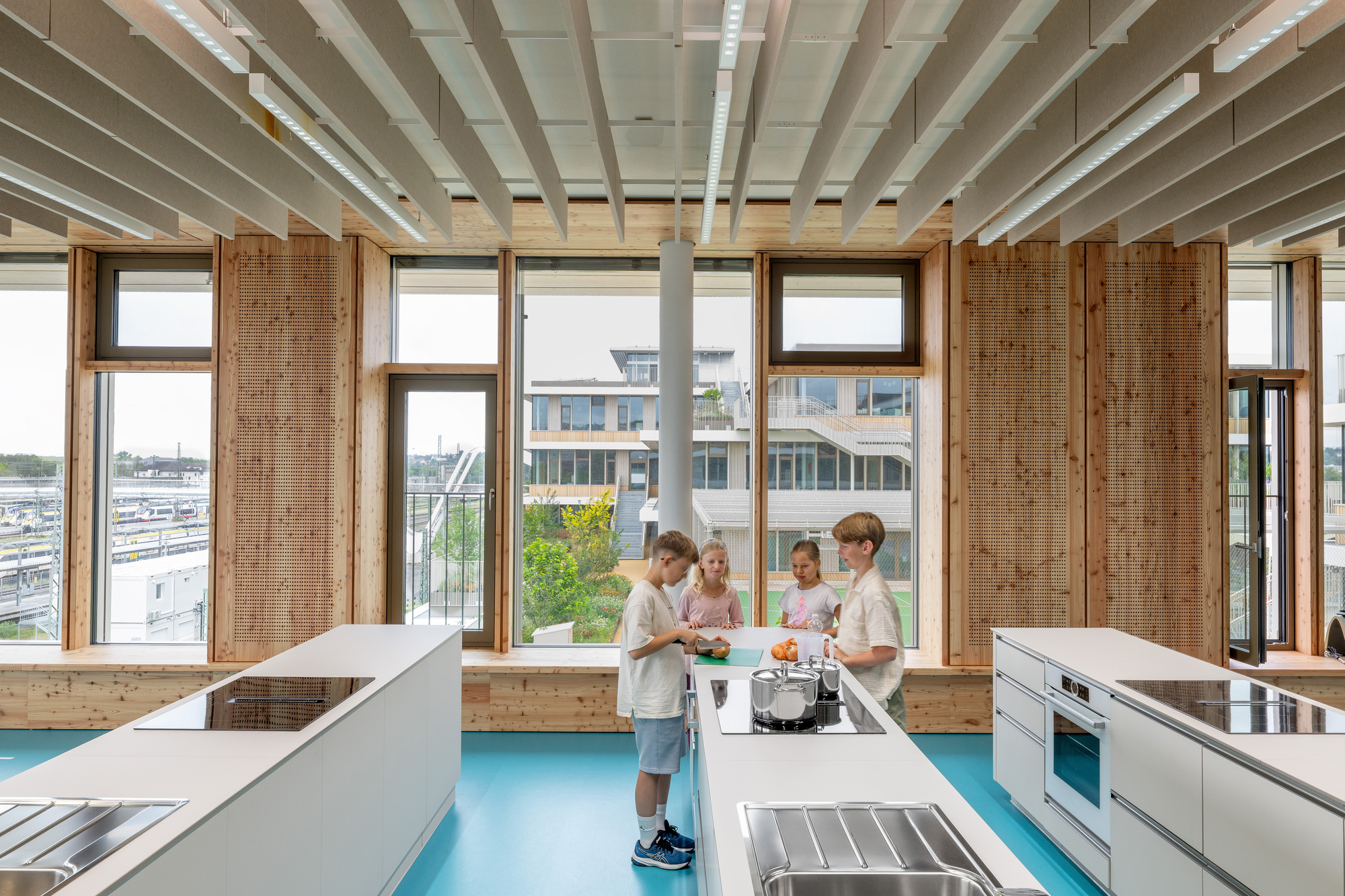 Teaching kitchen with white island counters, stainless appliances and perforated timber wall panels at the windows