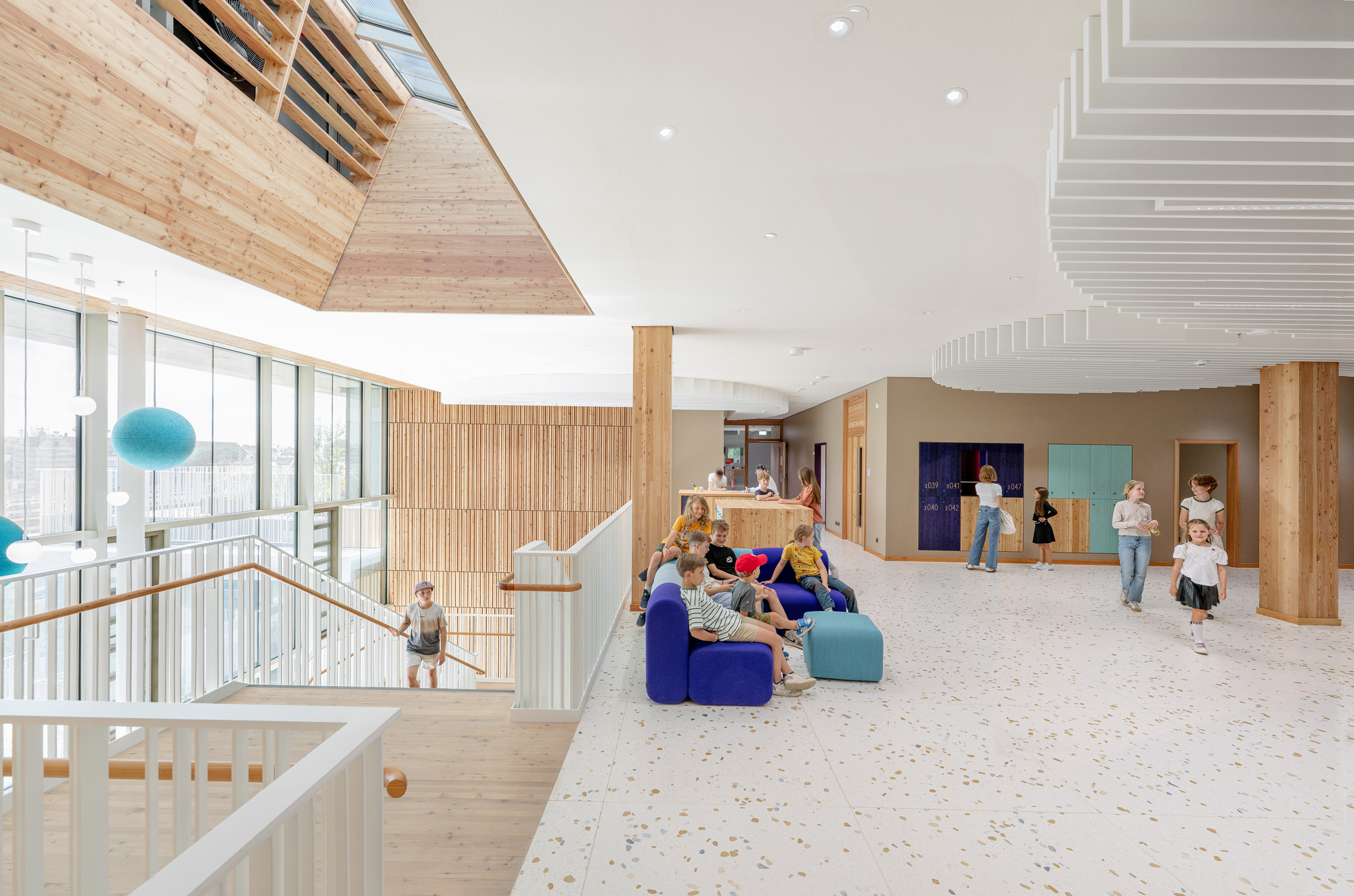 Double-height gathering space with angular timber skylight, timber slat walls and children on soft seating