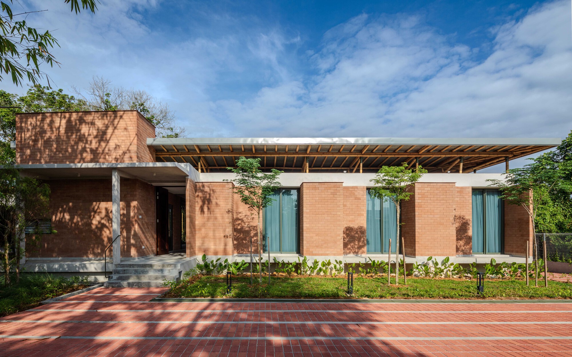 Brick facade with glass doors beneath a wide timber roof casting dappled shadows