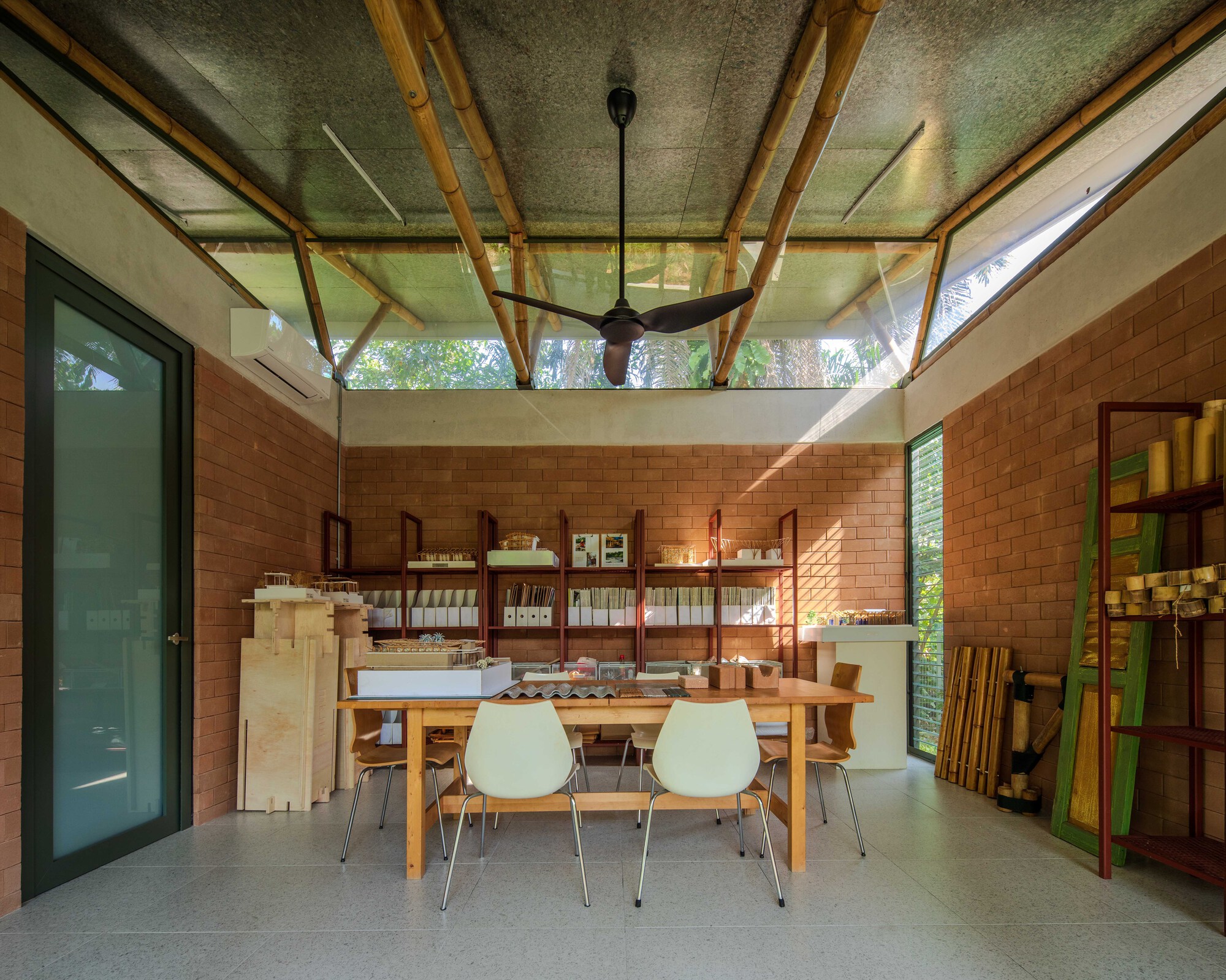 Workshop space with exposed timber roof structure, clerestory glazing, and red brick walls beneath dappled daylight