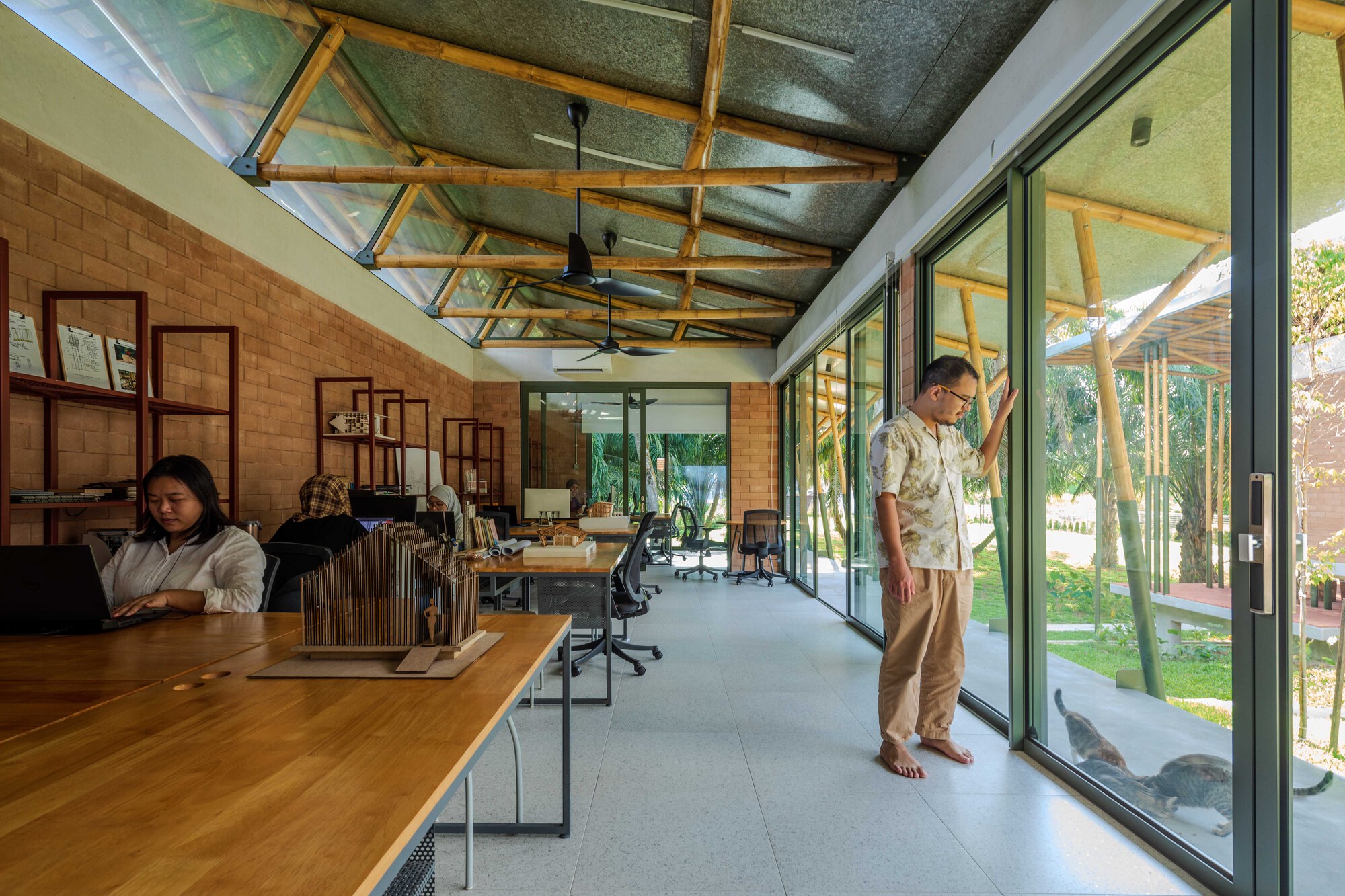 Studio interior with full-height sliding glass doors opening to a courtyard where two occupants work at timber desks