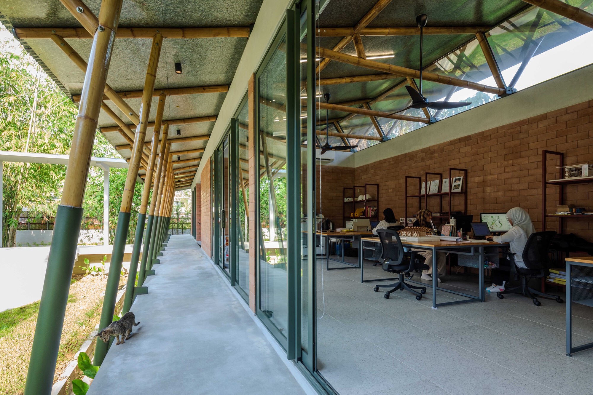 Covered walkway with timber columns and lattice roof beside sliding glass doors and a workspace occupied by several people