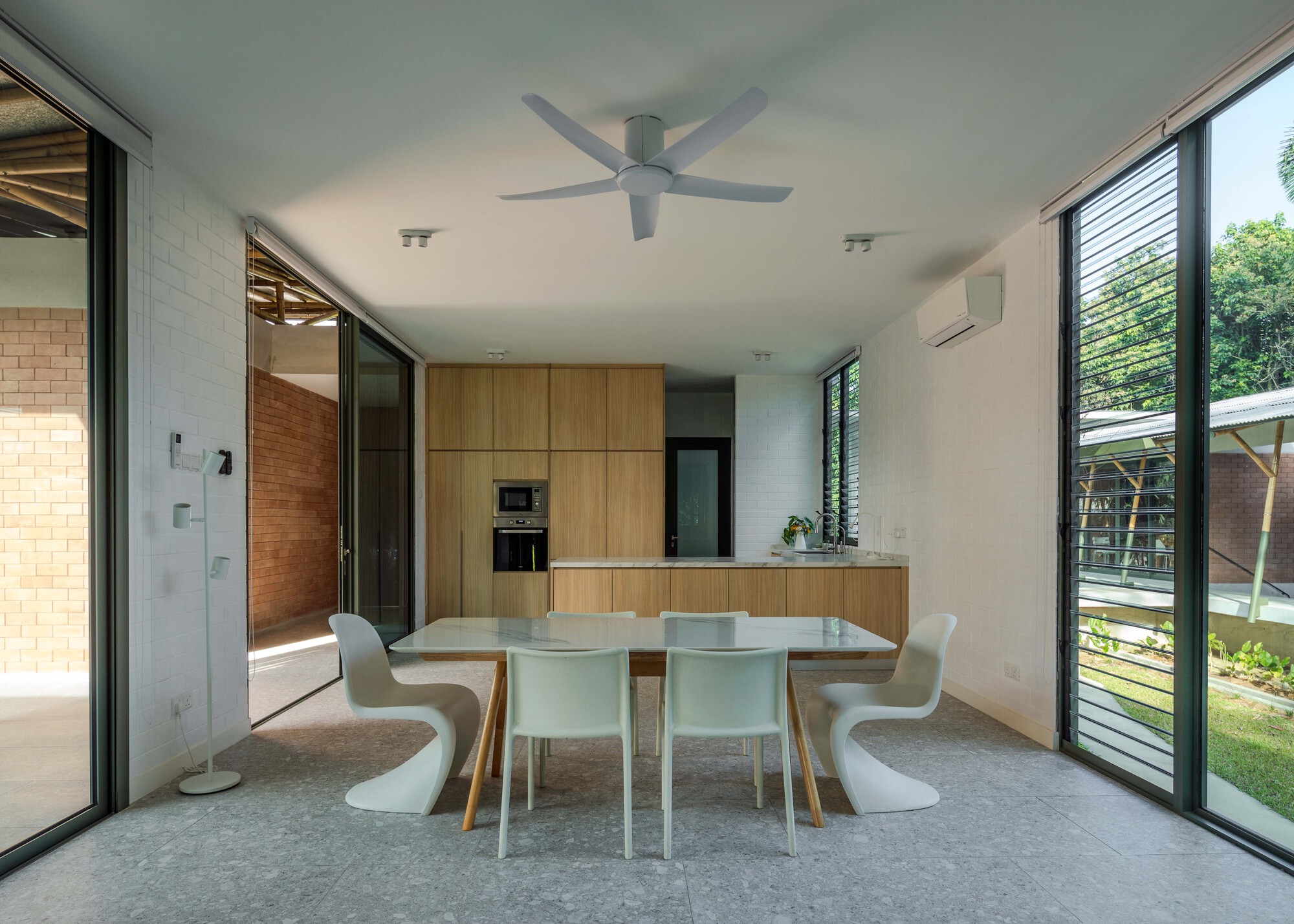 Open plan dining and kitchen space with timber cabinetry and corner glazing overlooking planted garden areas