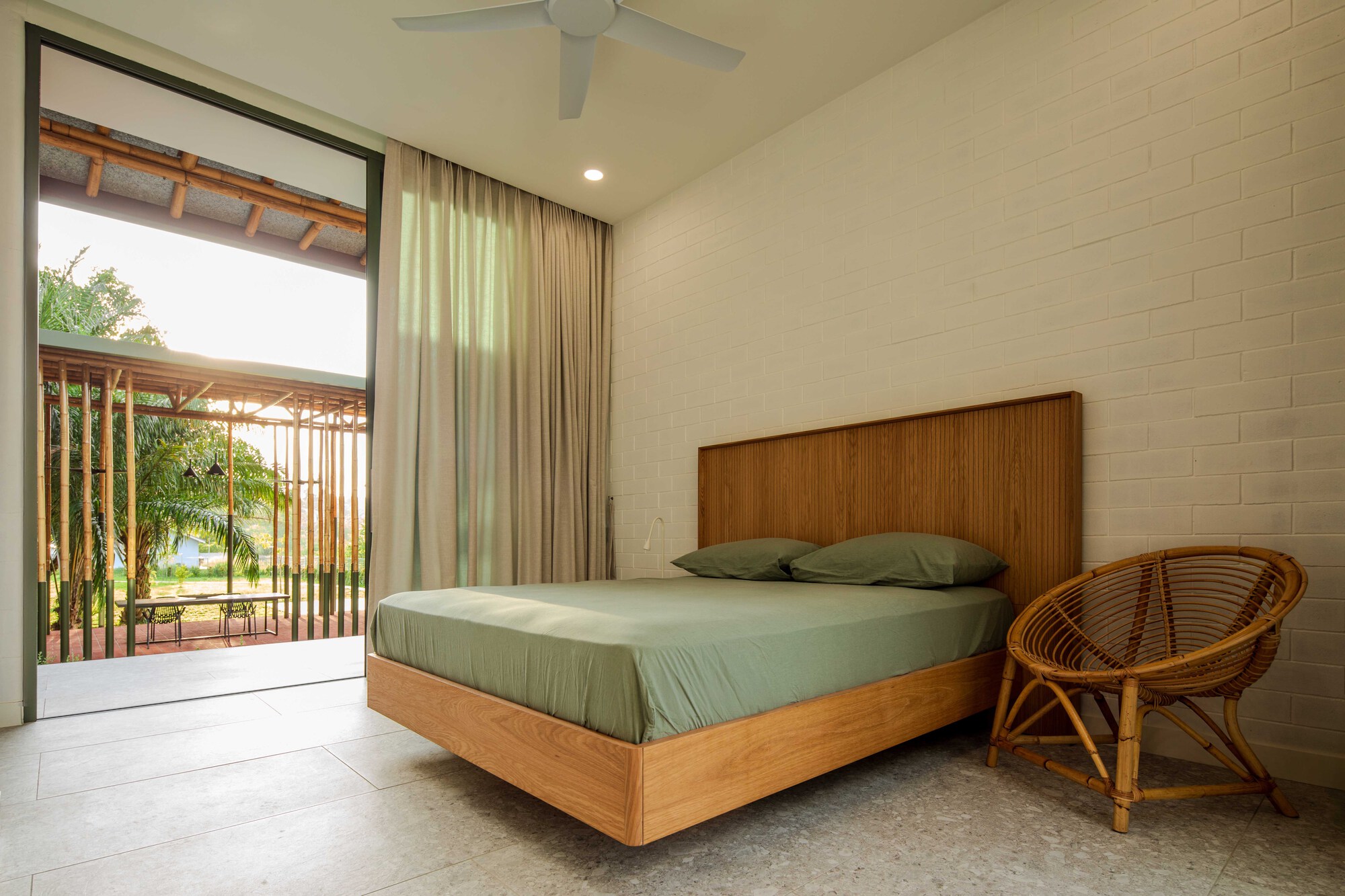 Bedroom with white brick wall and timber bed frame opening to vertical timber screen and greenery beyond