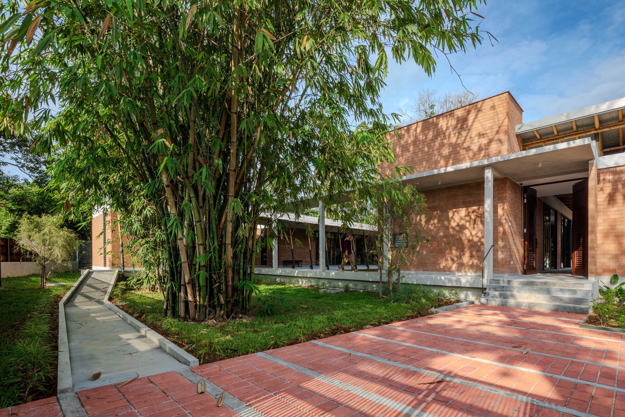 Red brick facade with overhanging roof beside bamboo grove and patterned tile courtyard