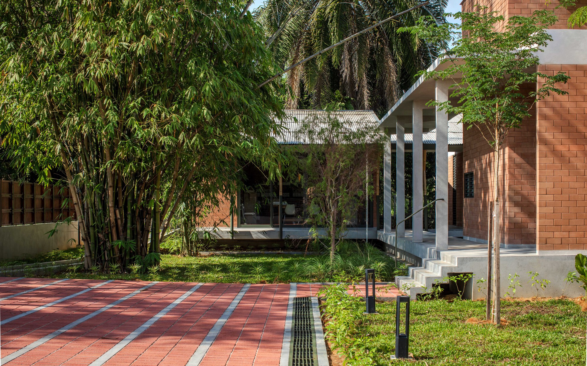 Covered pavilion with white columns and corrugated roof framed by bamboo and planted lawn