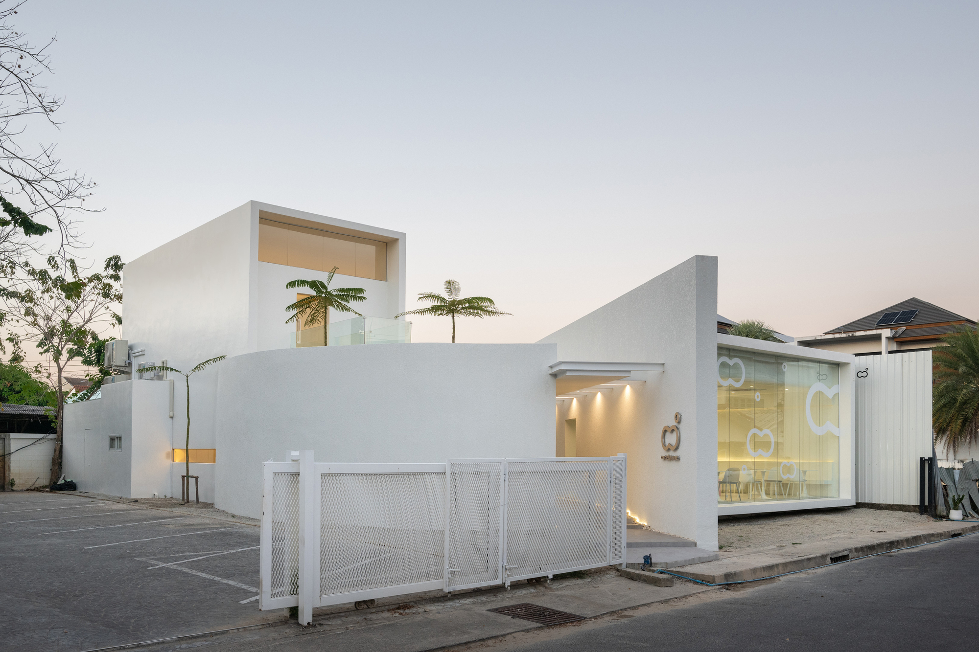 Street facade with white metal sliding gate and large corner glazing at twilight